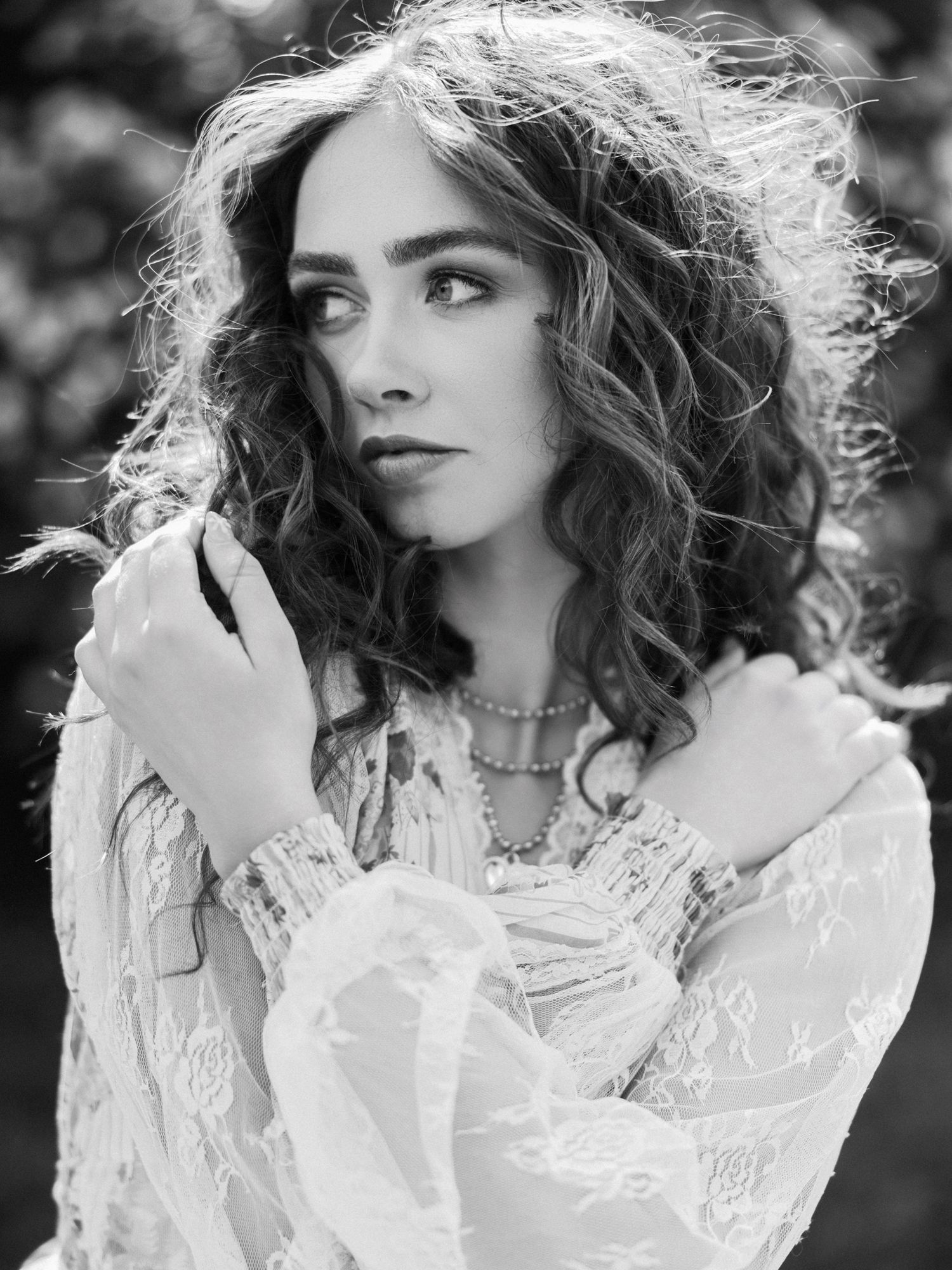 Black and white portrait of a woman in lace dress with curly hair and layered necklaces.
