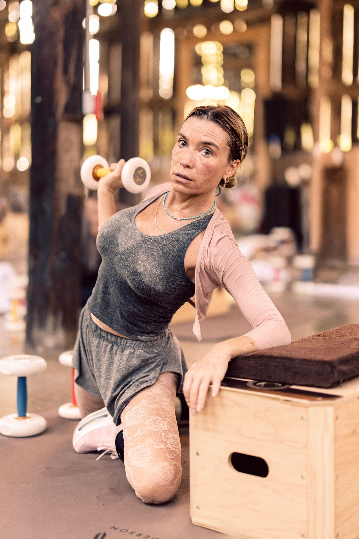Woman kneeling on gym floor lifting dumbbell during intense workout session in modern fitness center.