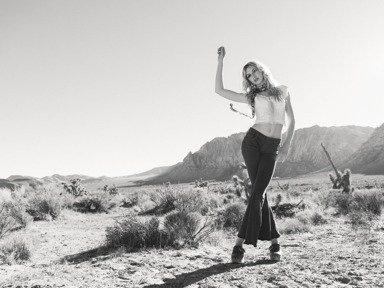 Black and white photo of a woman dancing freely in a vast desert landscape with mountains behind her.