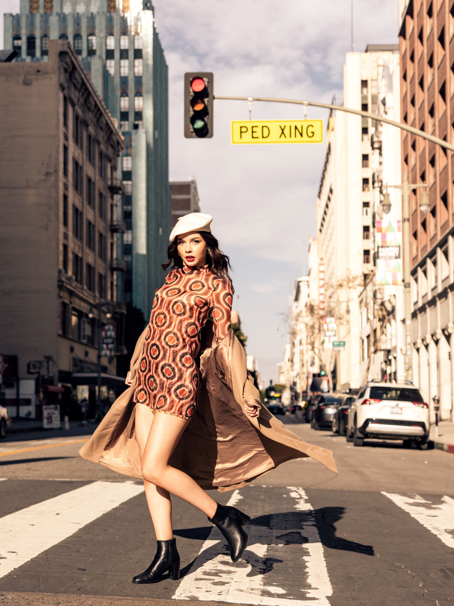 Stylish woman in patterned dress and beret crossing urban street intersection in downtown city.