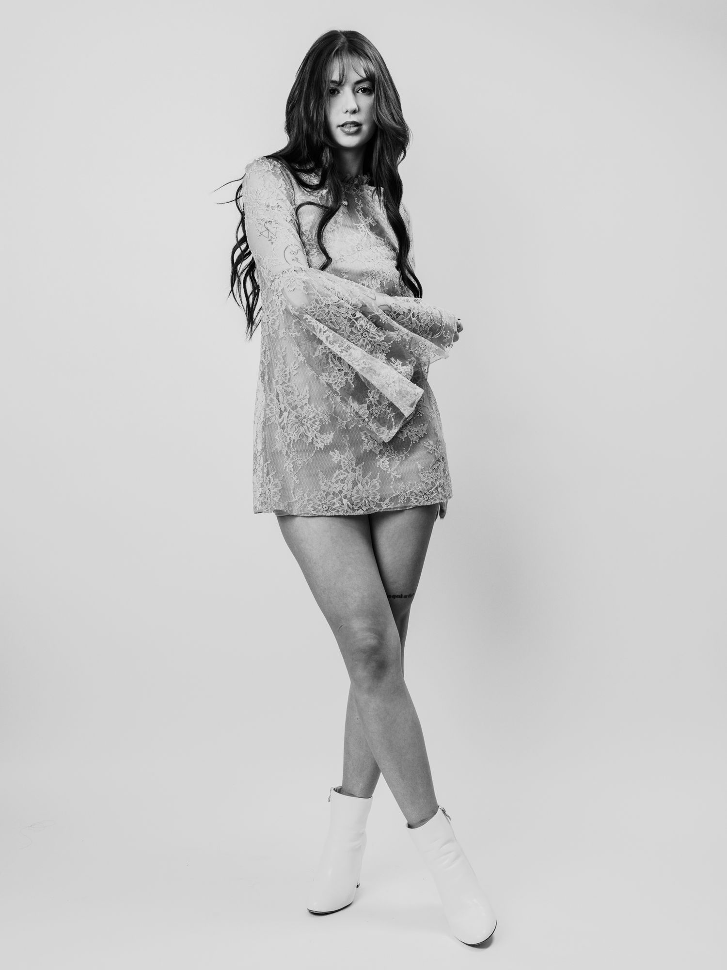 Black and white photo of a young woman in a mini dress and white boots, posing confidently in a studio setting.