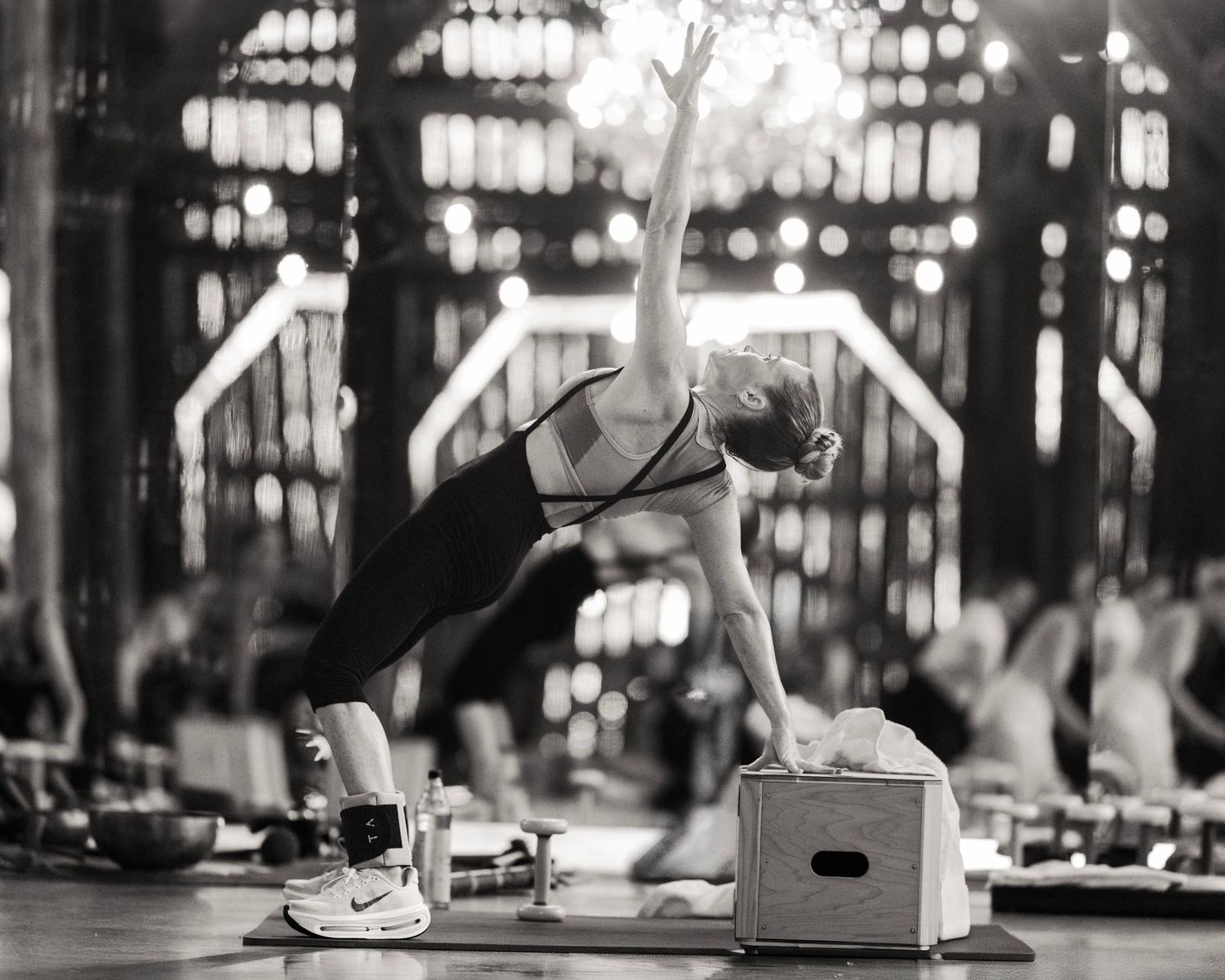 Woman performing a side plank yoga pose on a mat in a dimly lit studio during a group fitness class.