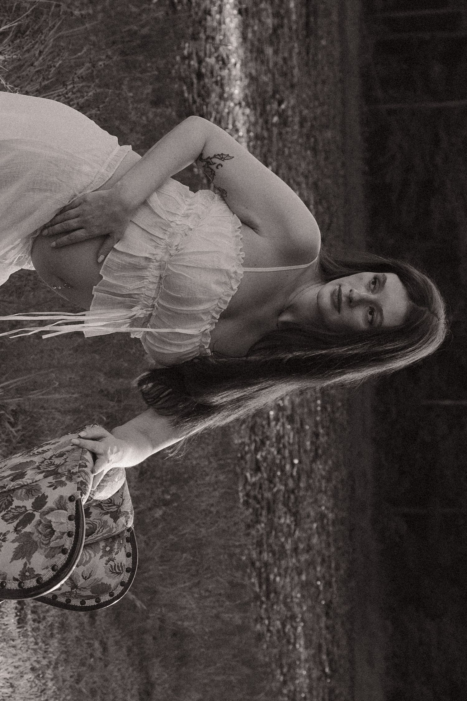 Black and white portrait of a young woman in a white dress holding a guitar in a natural setting.