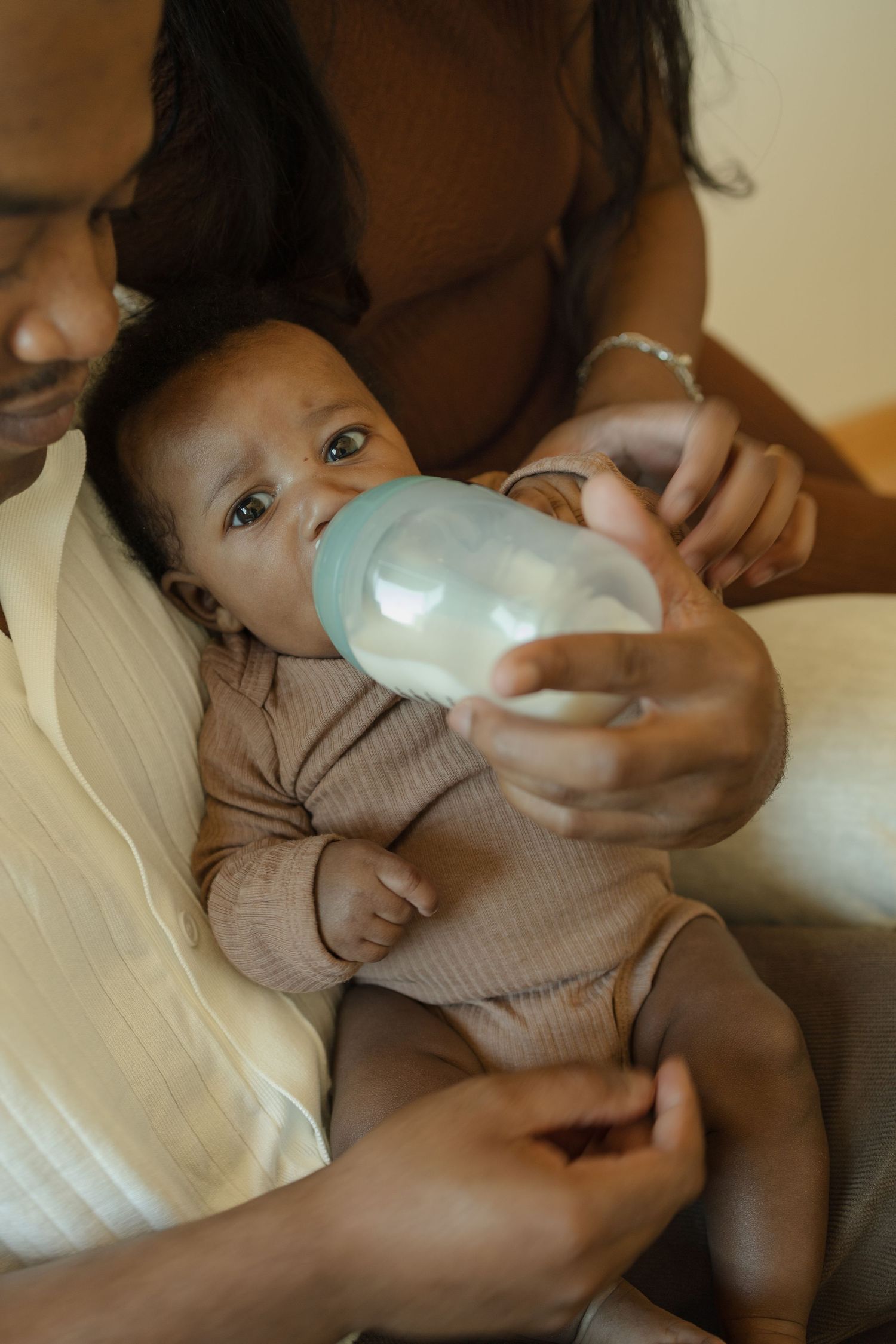 Parents bottle feeding their newborn baby in a warm, intimate moment at home.