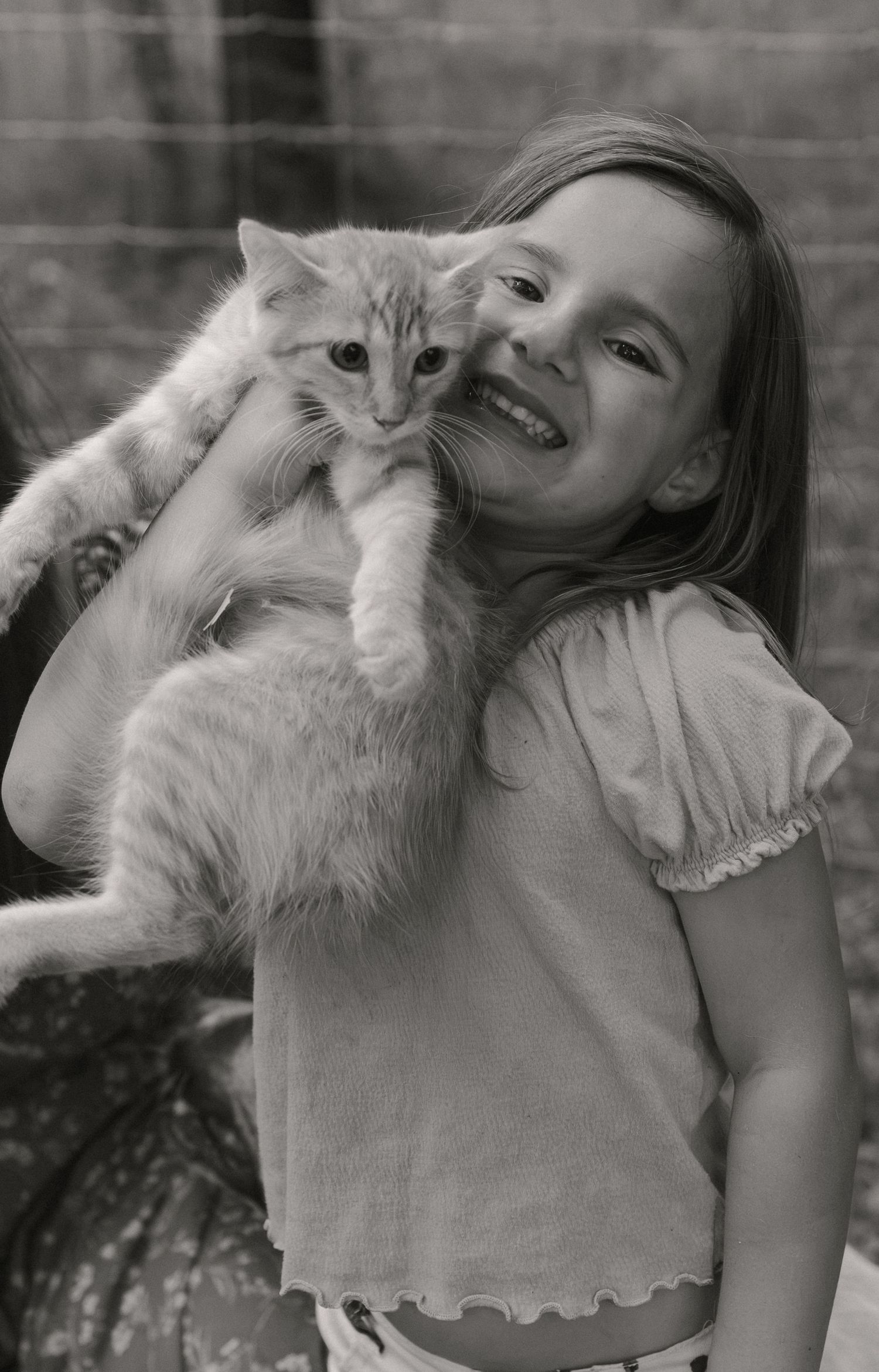 Young girl smiling and holding a fluffy kitten on her shoulder in a black and white photo.