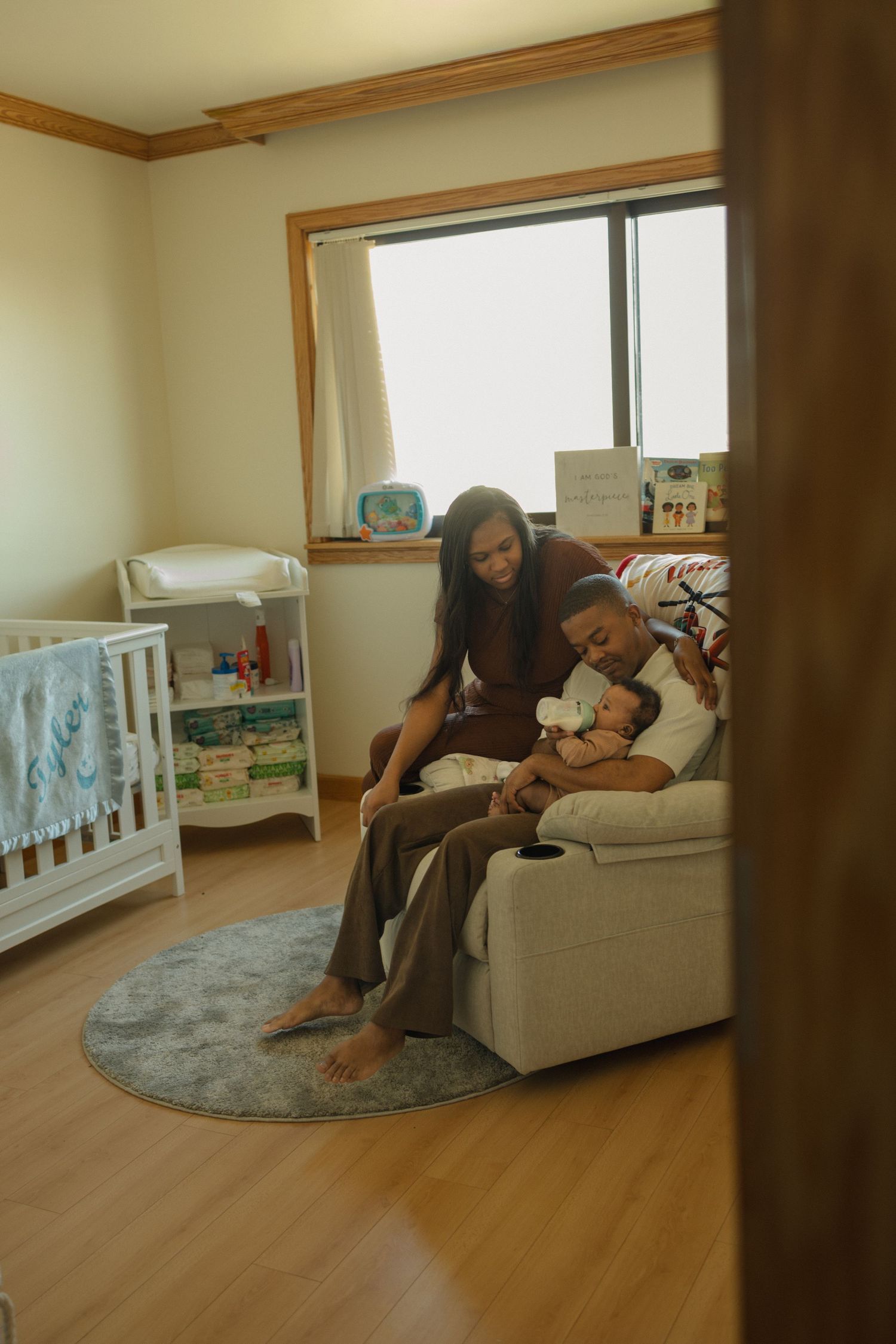 Young family bonding with newborn in a cozy nursery room with crib and natural light.