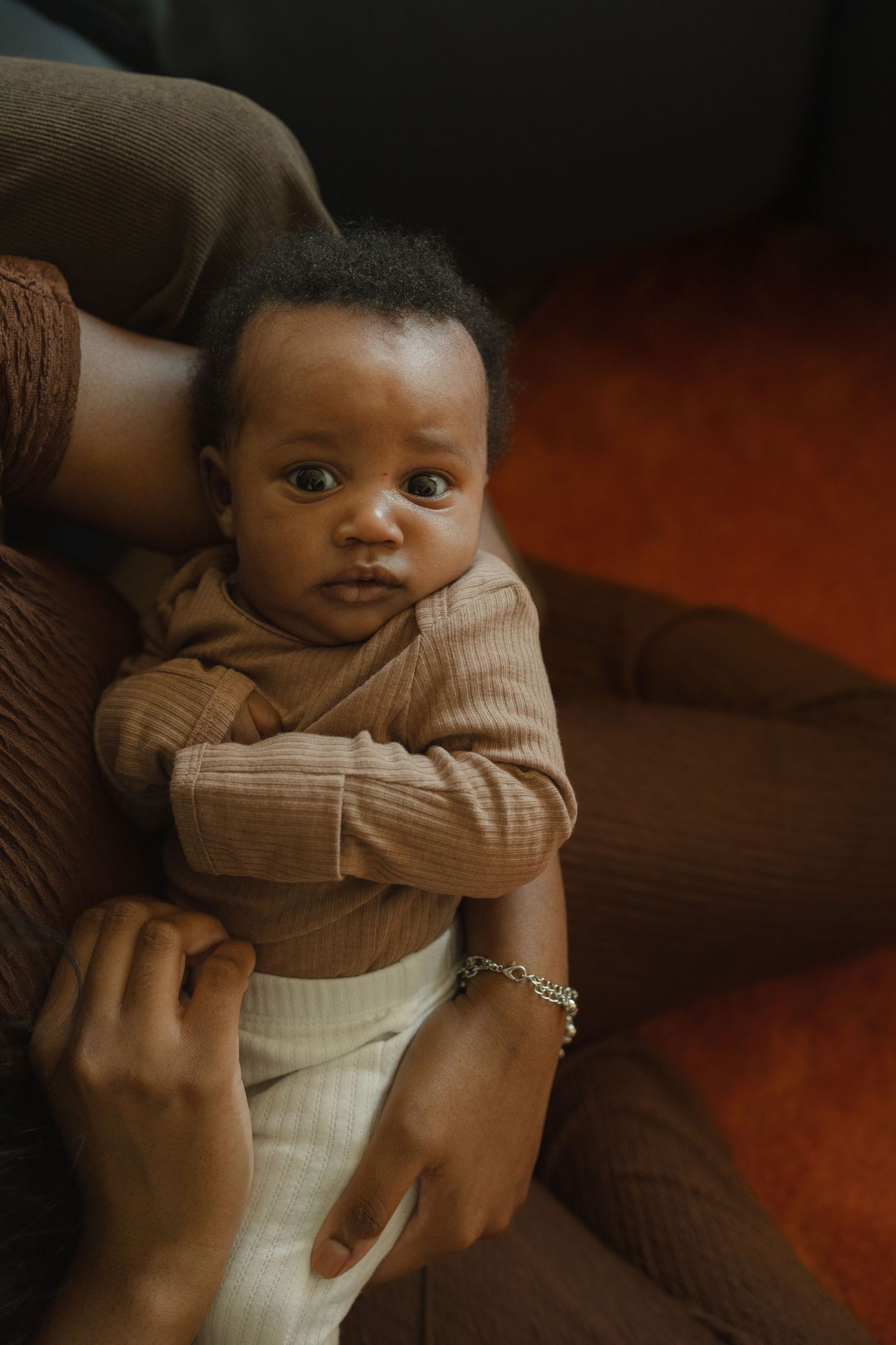 Adorable Black baby in brown ribbed onesie being held by parent on a cozy couch. In Southern Pines NC.