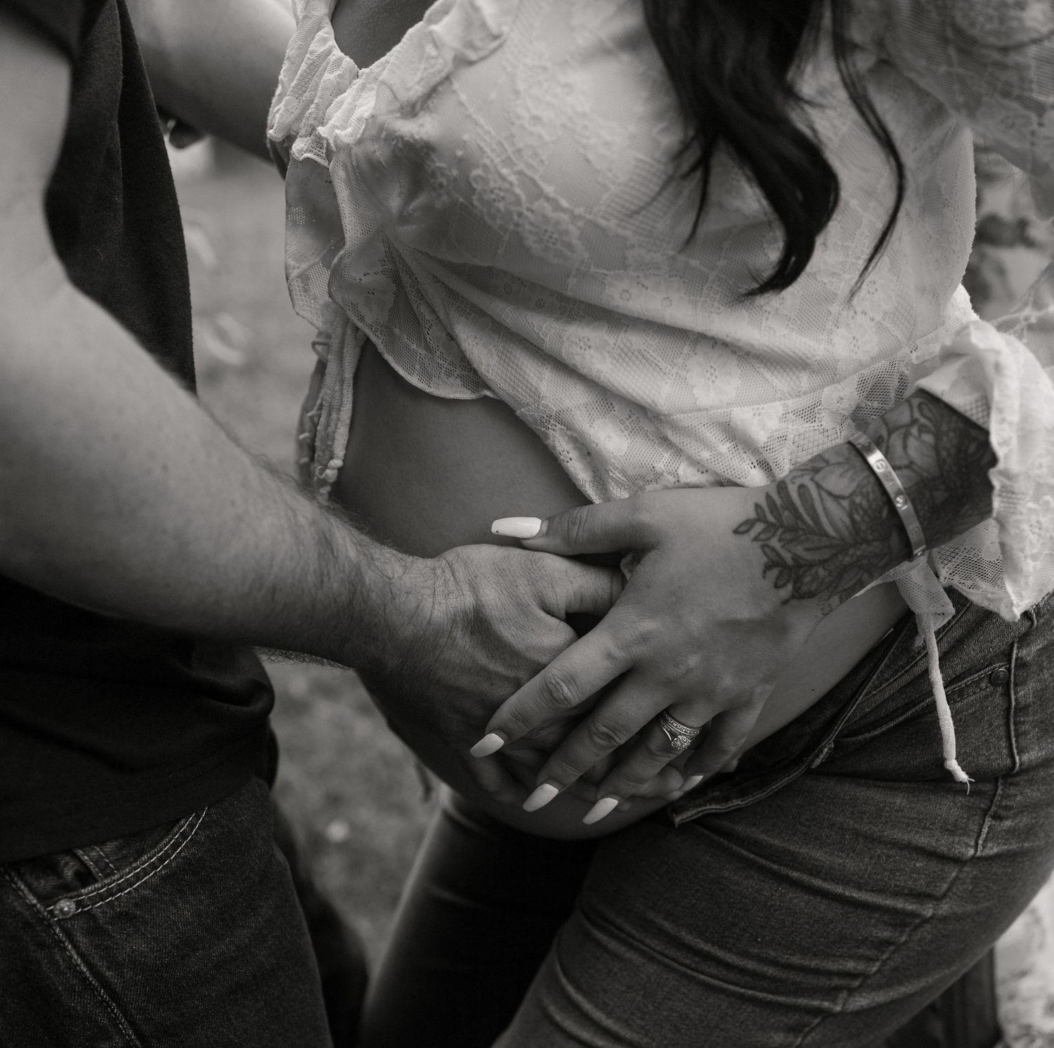 Black and white close-up of couple's tattooed hands cradling pregnant belly.