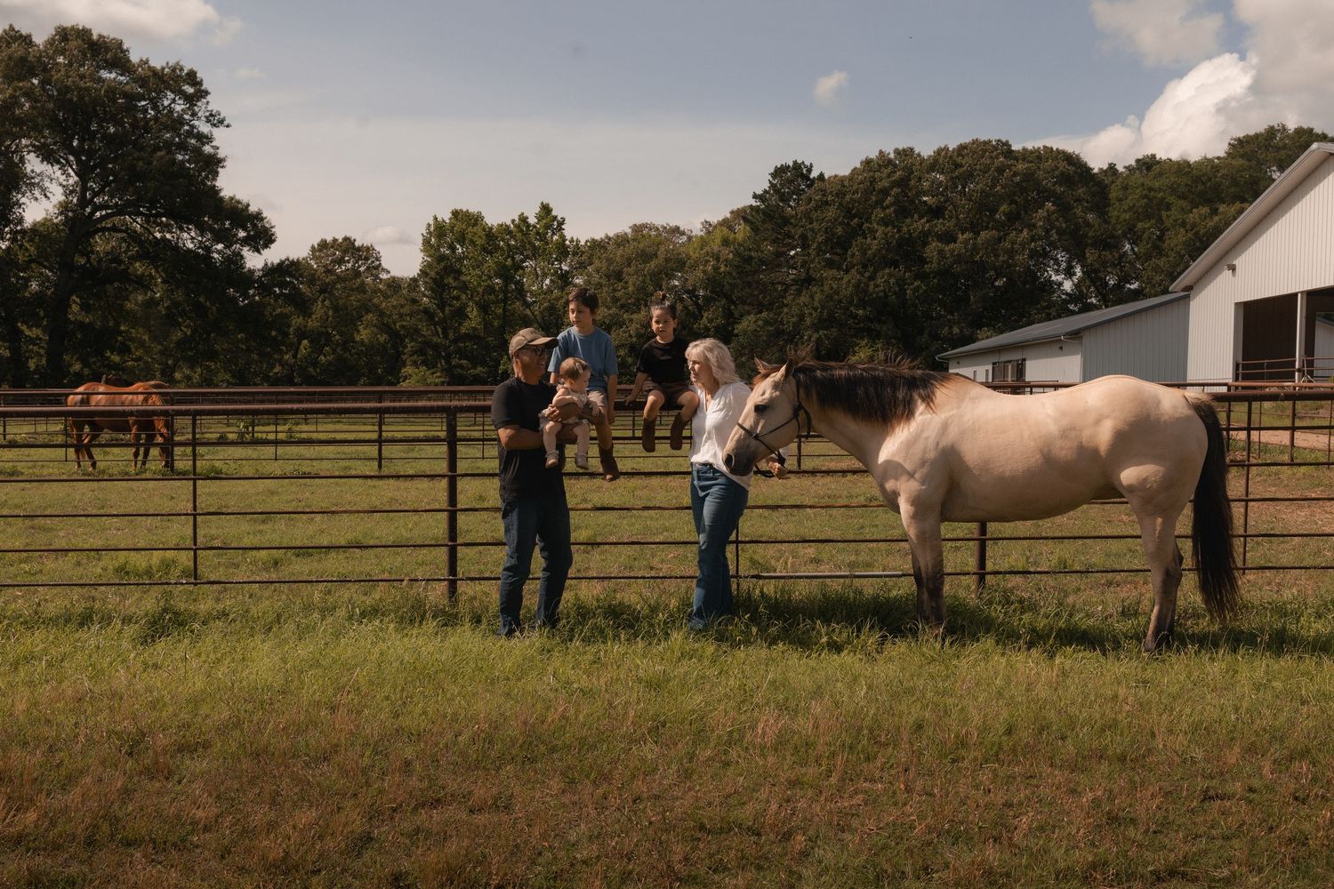 Family interacting with a horse in a fenced pasture on a partly cloudy day.