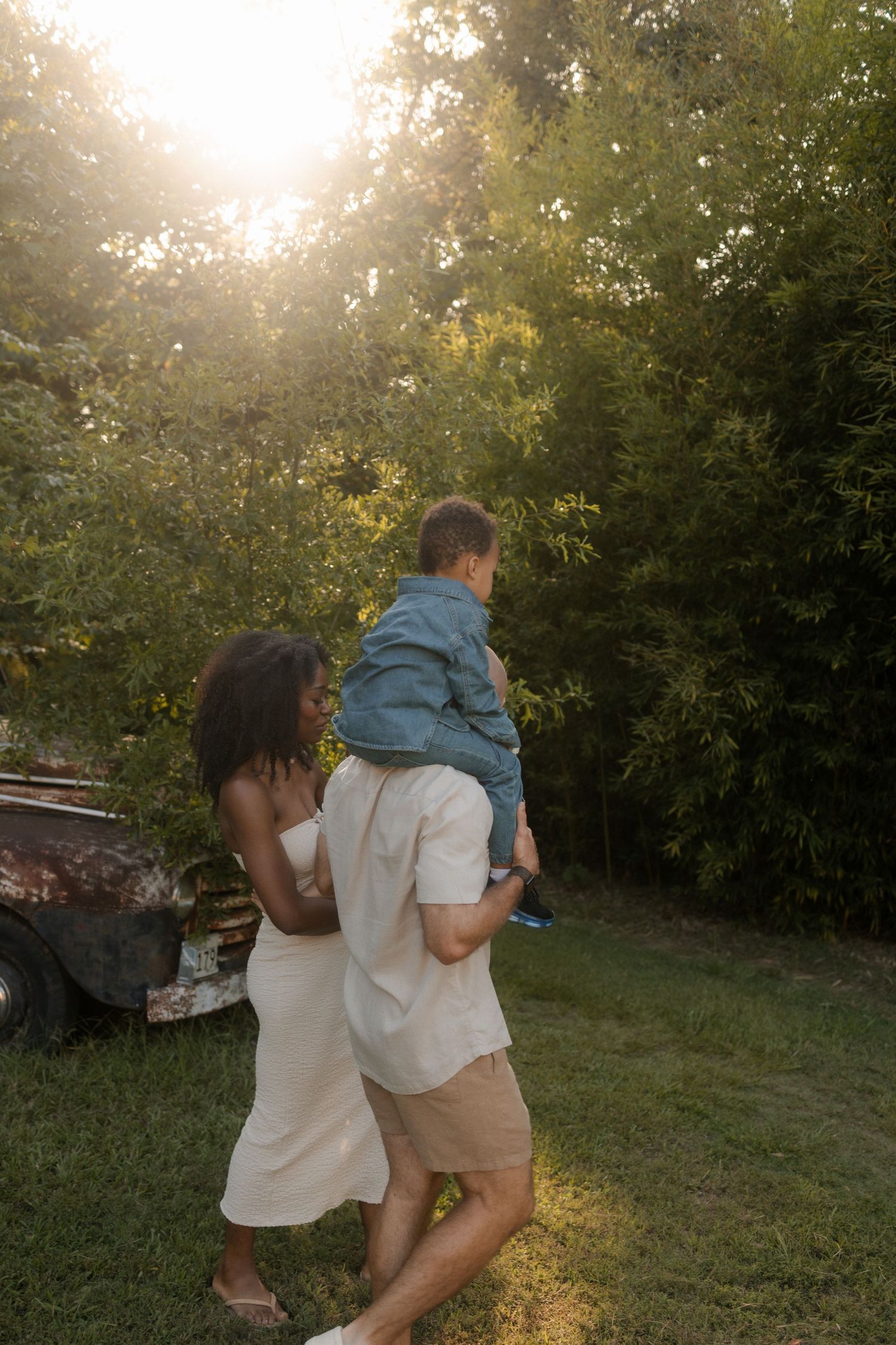 A family enjoys golden hour outdoors as a father carries his young son while mother walks beside them.