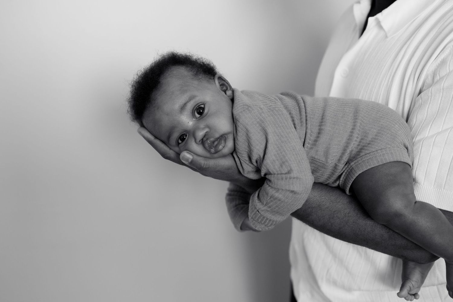 Black and white photo of father holding newborn baby securely in one arm against wall.