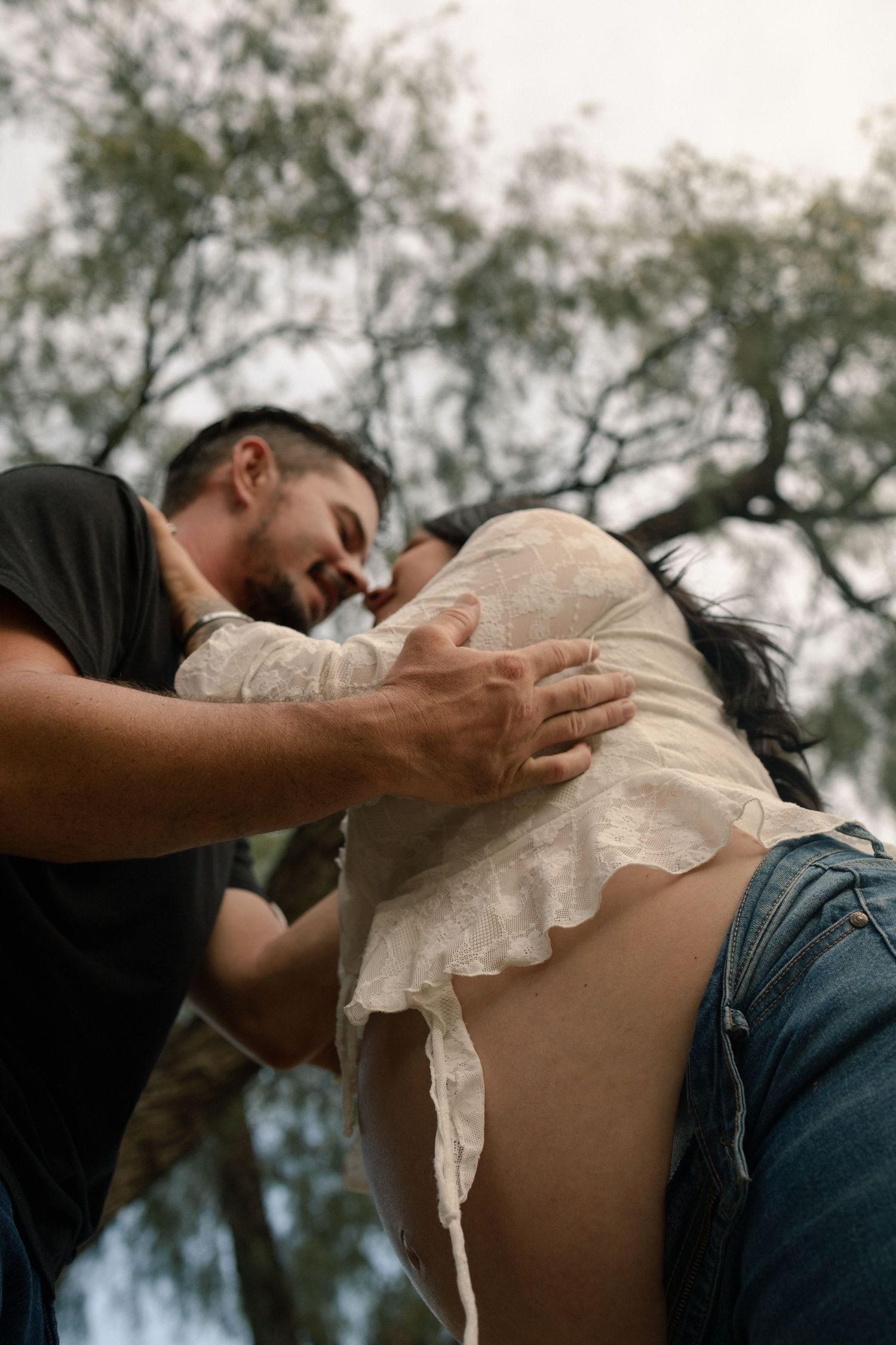 A couple shares an intimate moment outdoors, with the man tenderly touching the womans pregnant belly.