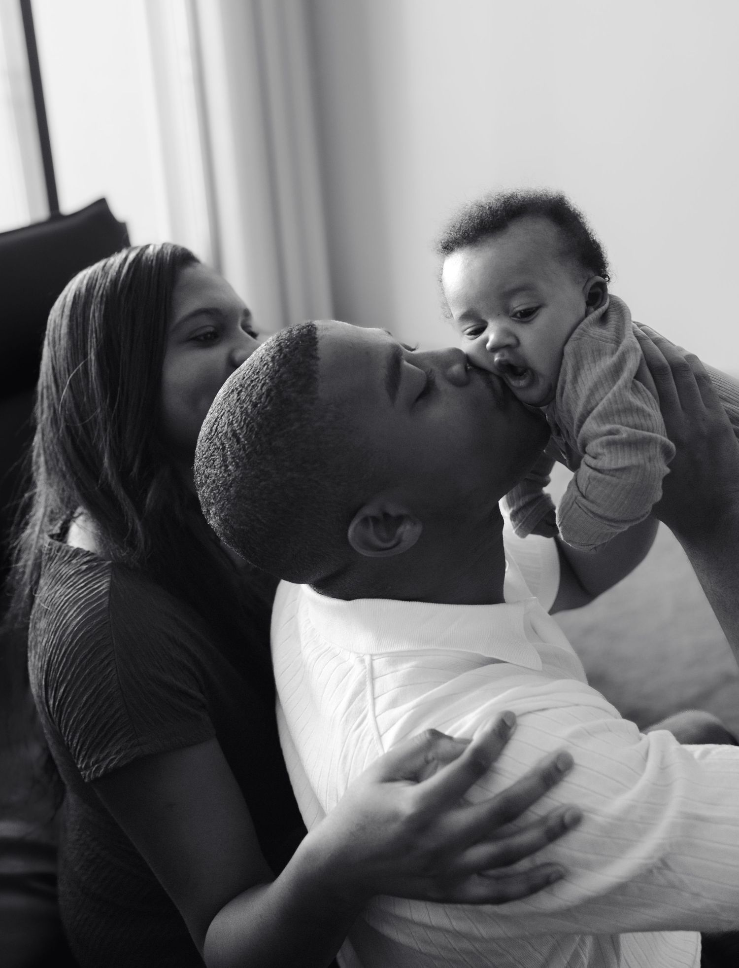 Black and white photo of loving parents kissing and playing with their laughing baby.