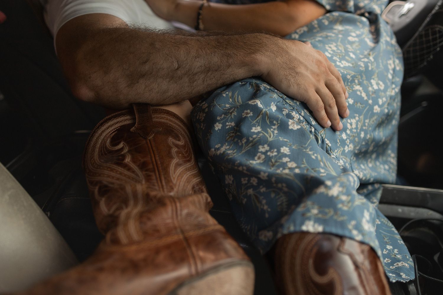Close-up of a couple sitting together, man's hand resting on woman's floral dress with cowboy boots.