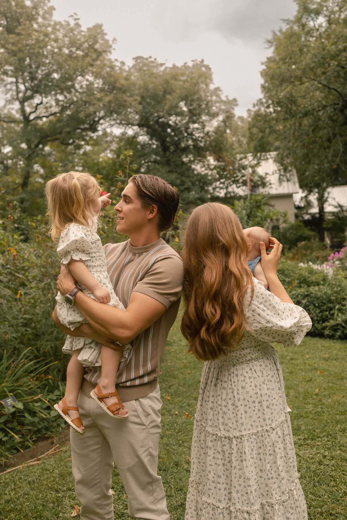 A couple holding two young children share a joyful moment together in a beautiful green garden.