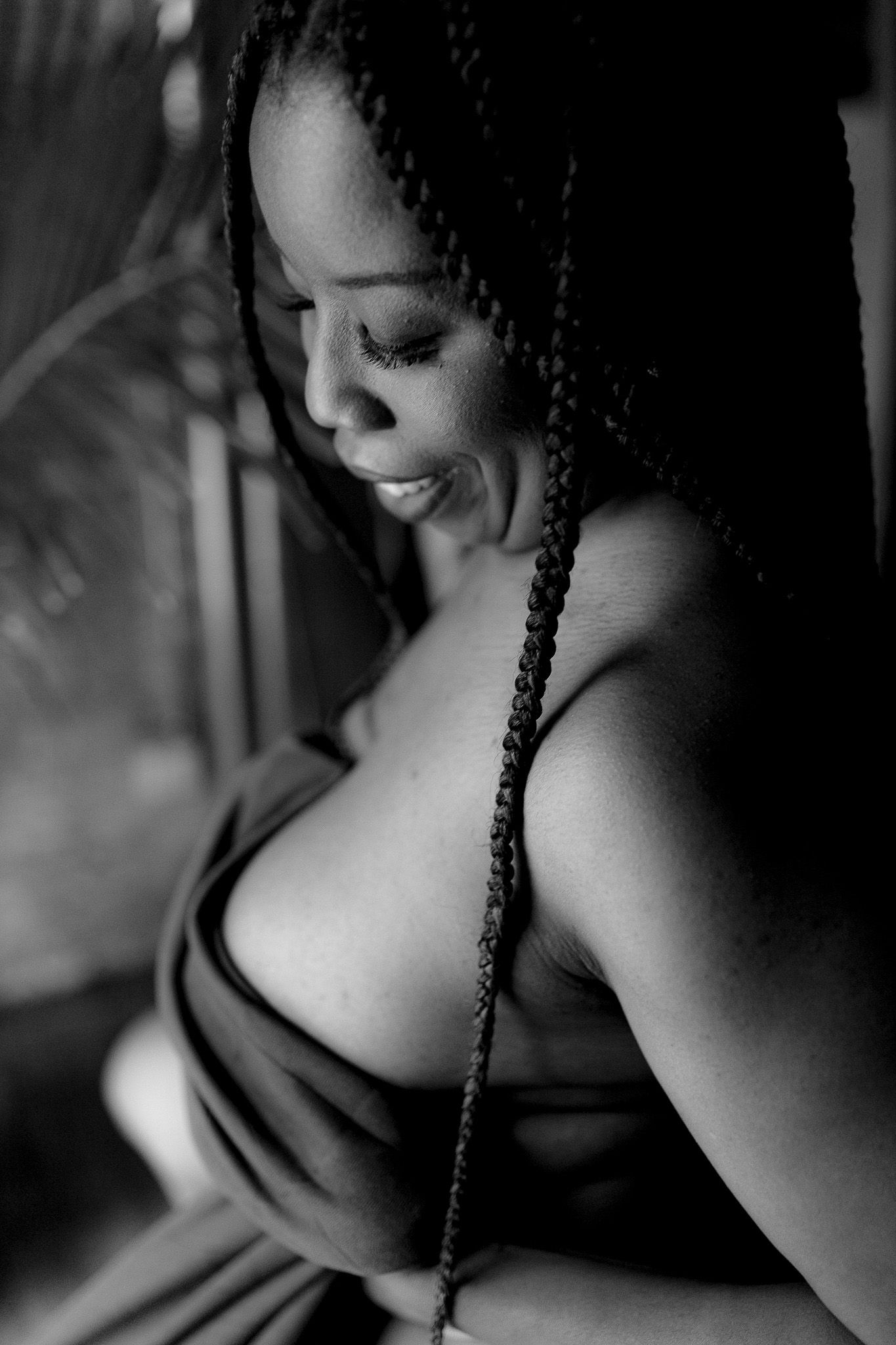 Black and white close-up boudoir portrait of a smiling woman with long box braids in a wrap top.