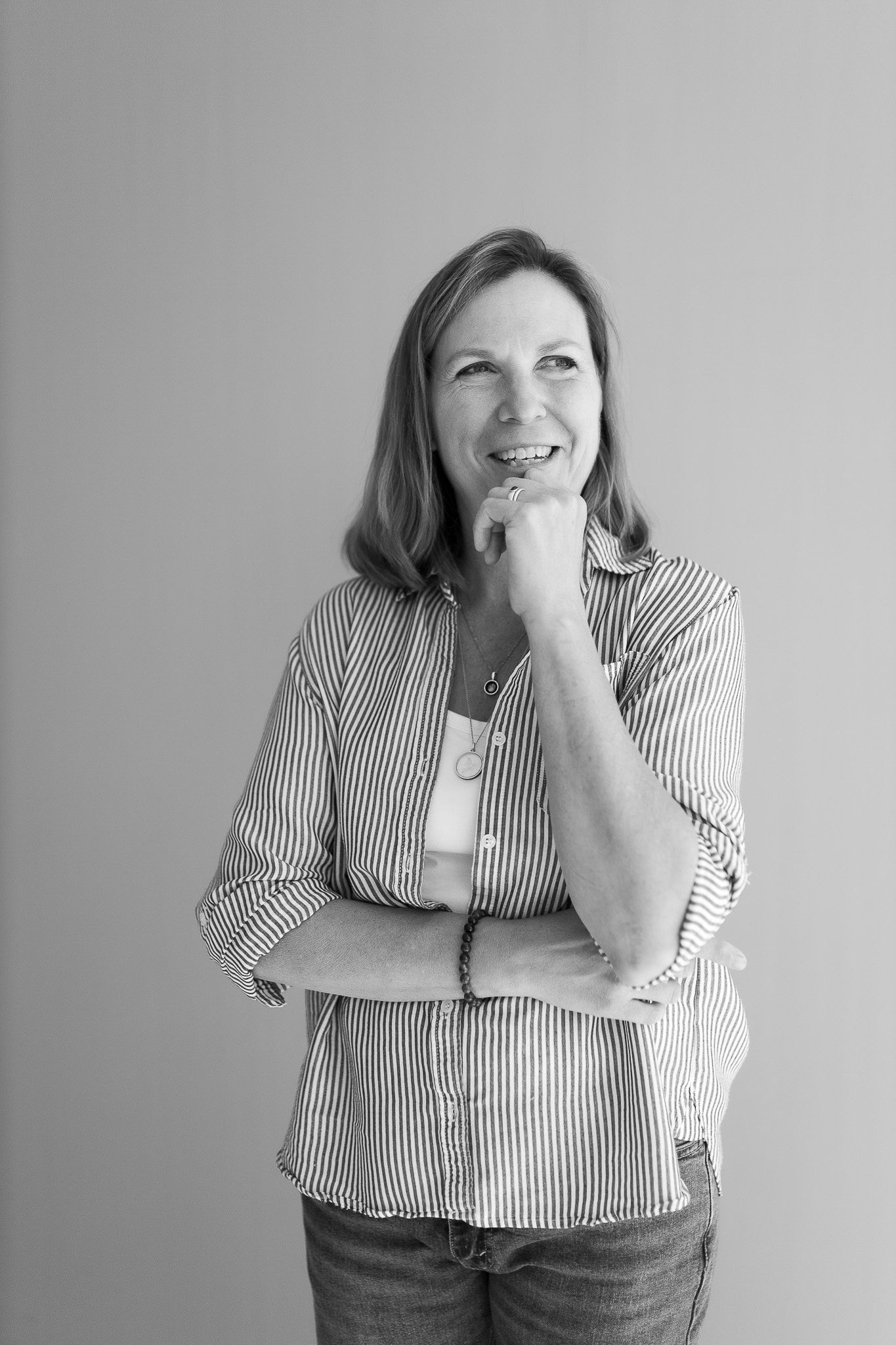 Woman in striped shirt smiling with hand on chin in thoughtful black and white studio portrait.