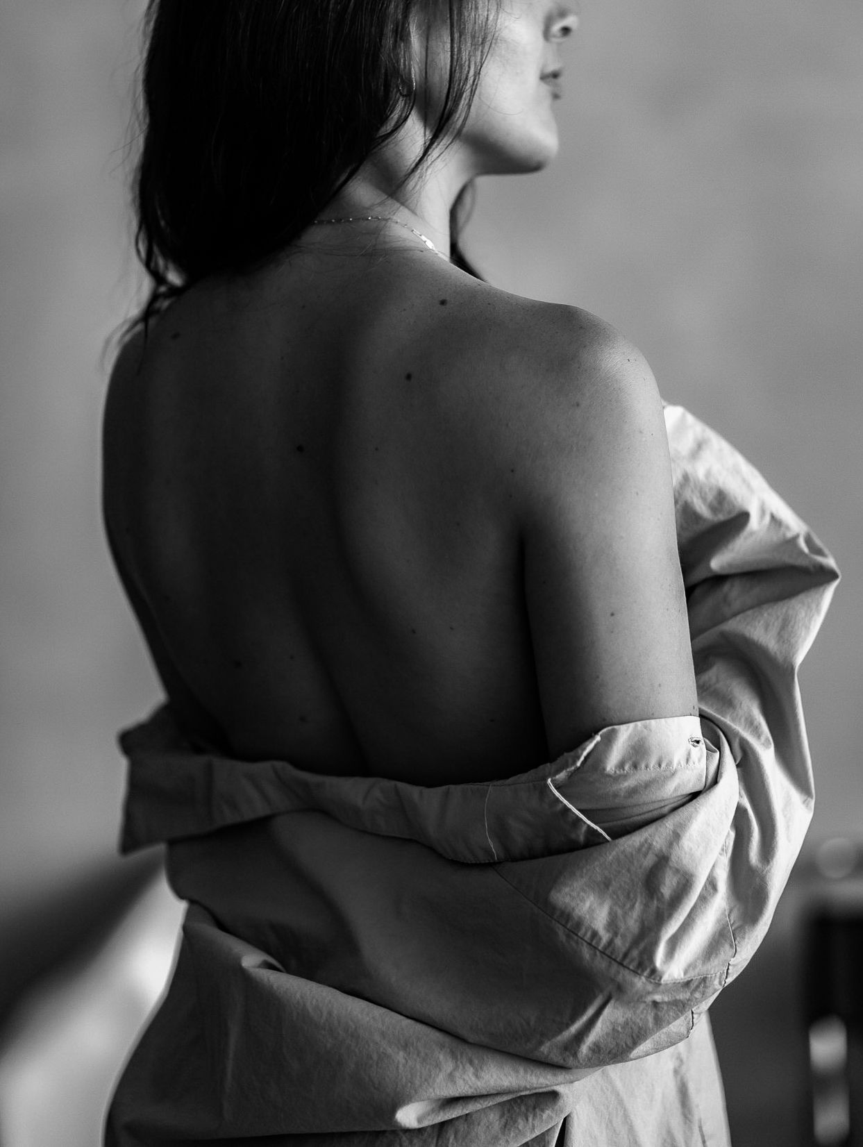 Black and white artistic photo of a womans bare back with a loosely worn linen shirt.