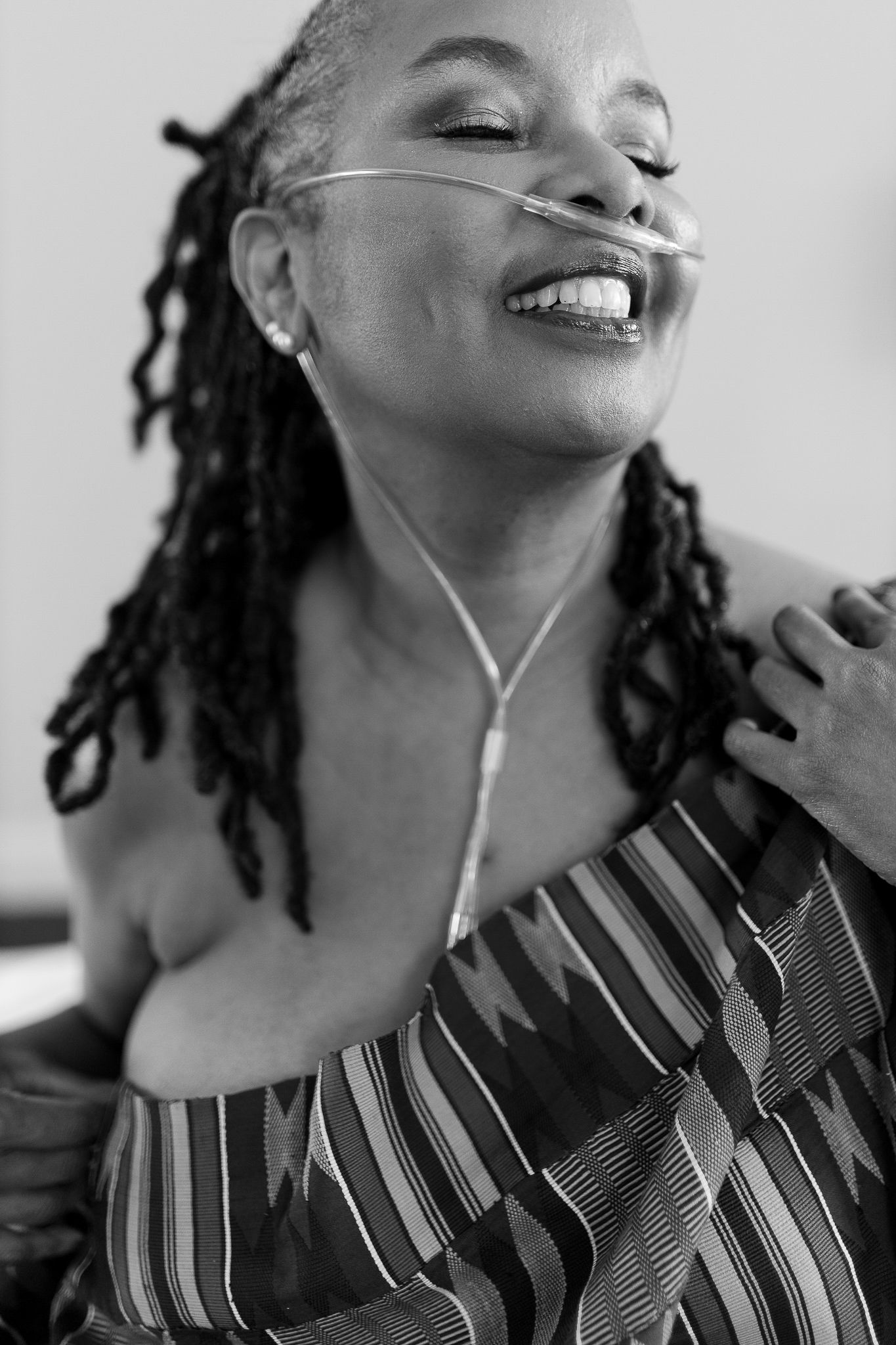 Joyful woman with locs wearing nasal cannula and striped off-shoulder top laughing in black and white.