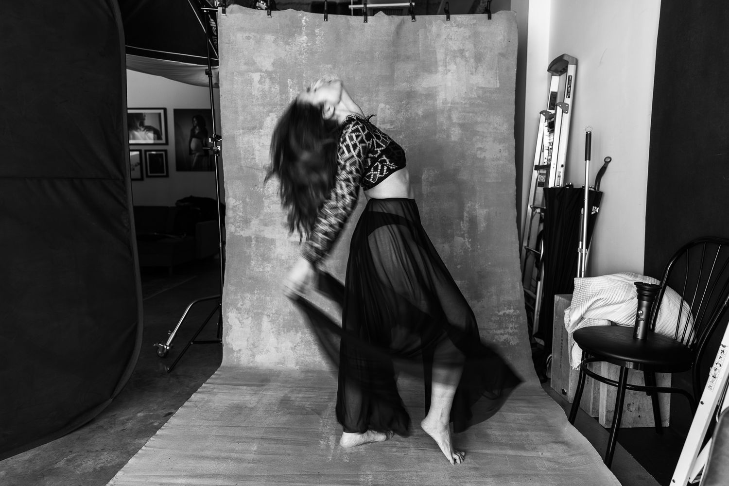 Black and white motion blur image of a woman spinning in a black flowing skirt in a photography studio.