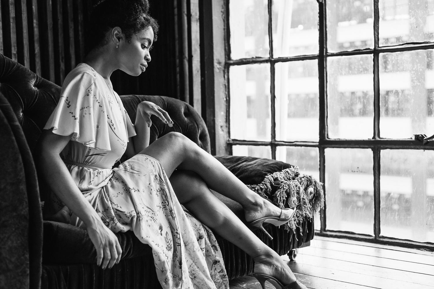 Young woman in white dress sitting pensively by large window in armchair, black and white photo.