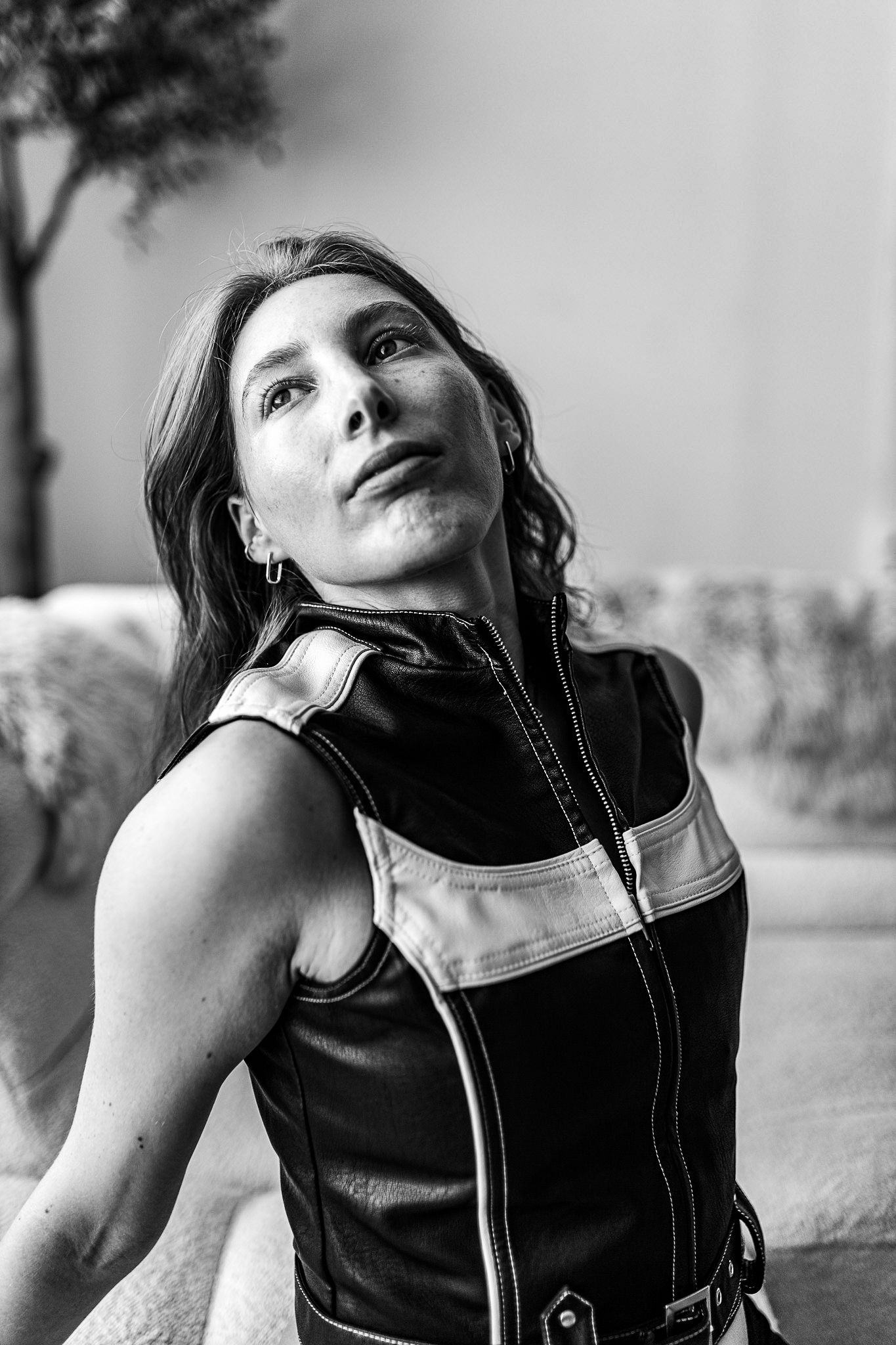 Woman in black leather vest looking upward in dramatic black and white portrait.