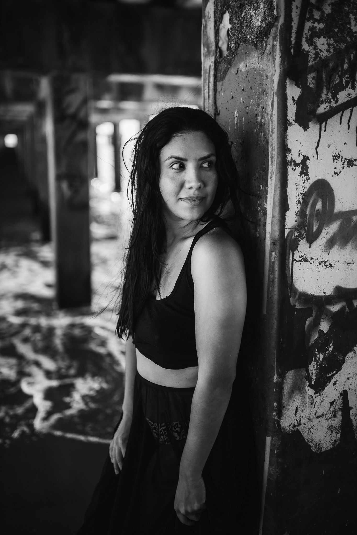 Black and white portrait of a woman in a black crop top leaning against a graffiti-covered wall.