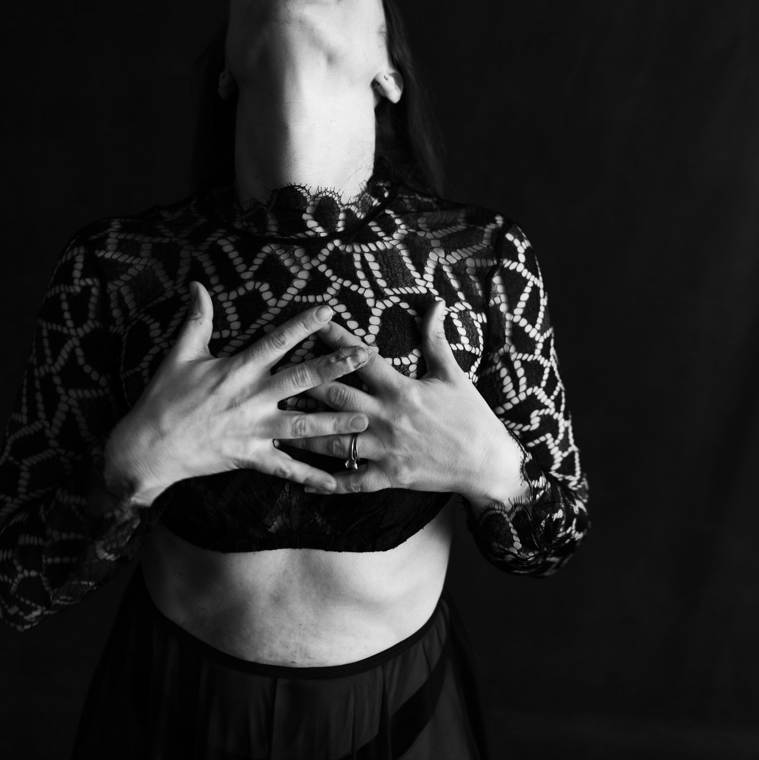 Close-up of woman in patterned black top with hands on chest, black and white studio photo.