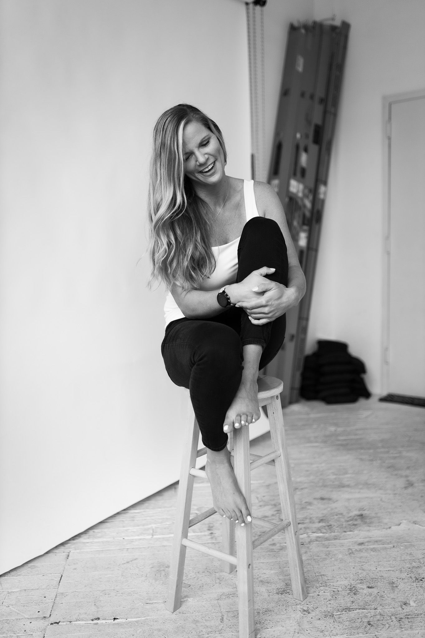 Black and white photo of laughing blonde woman posing on wooden stool.