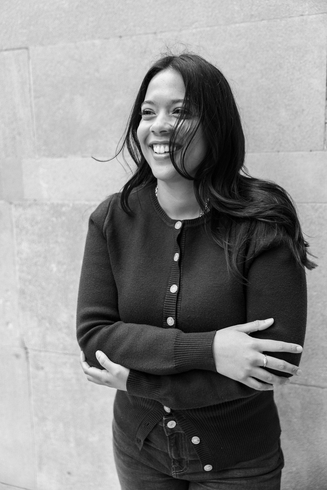 Black and white portrait of a smiling young woman with long dark hair, wearing a cardigan, arms crossed.