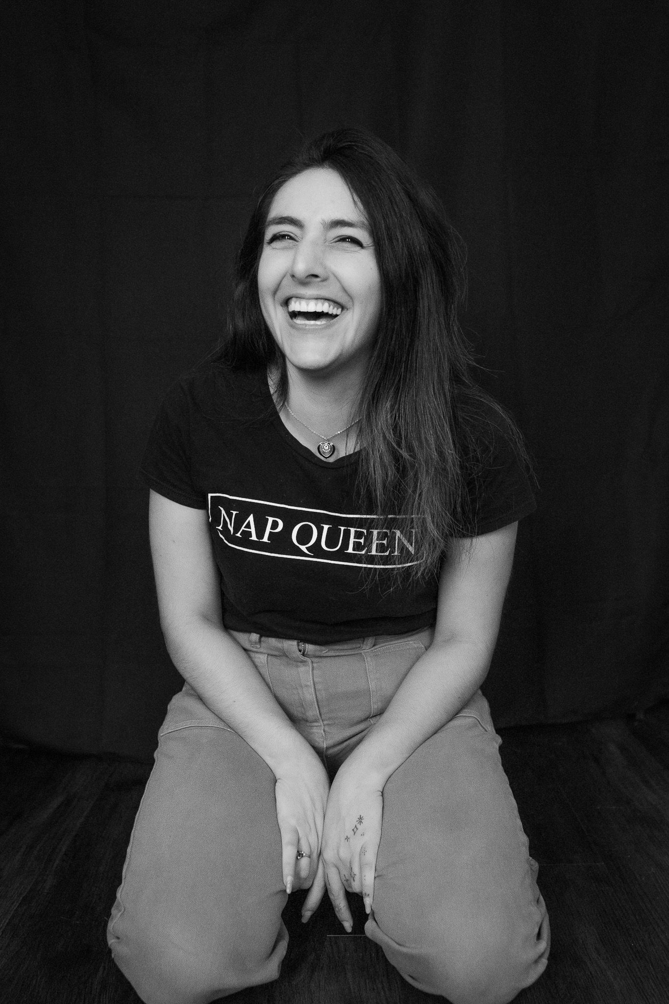 Woman in NAP QUEEN t-shirt laughing while sitting on floor.