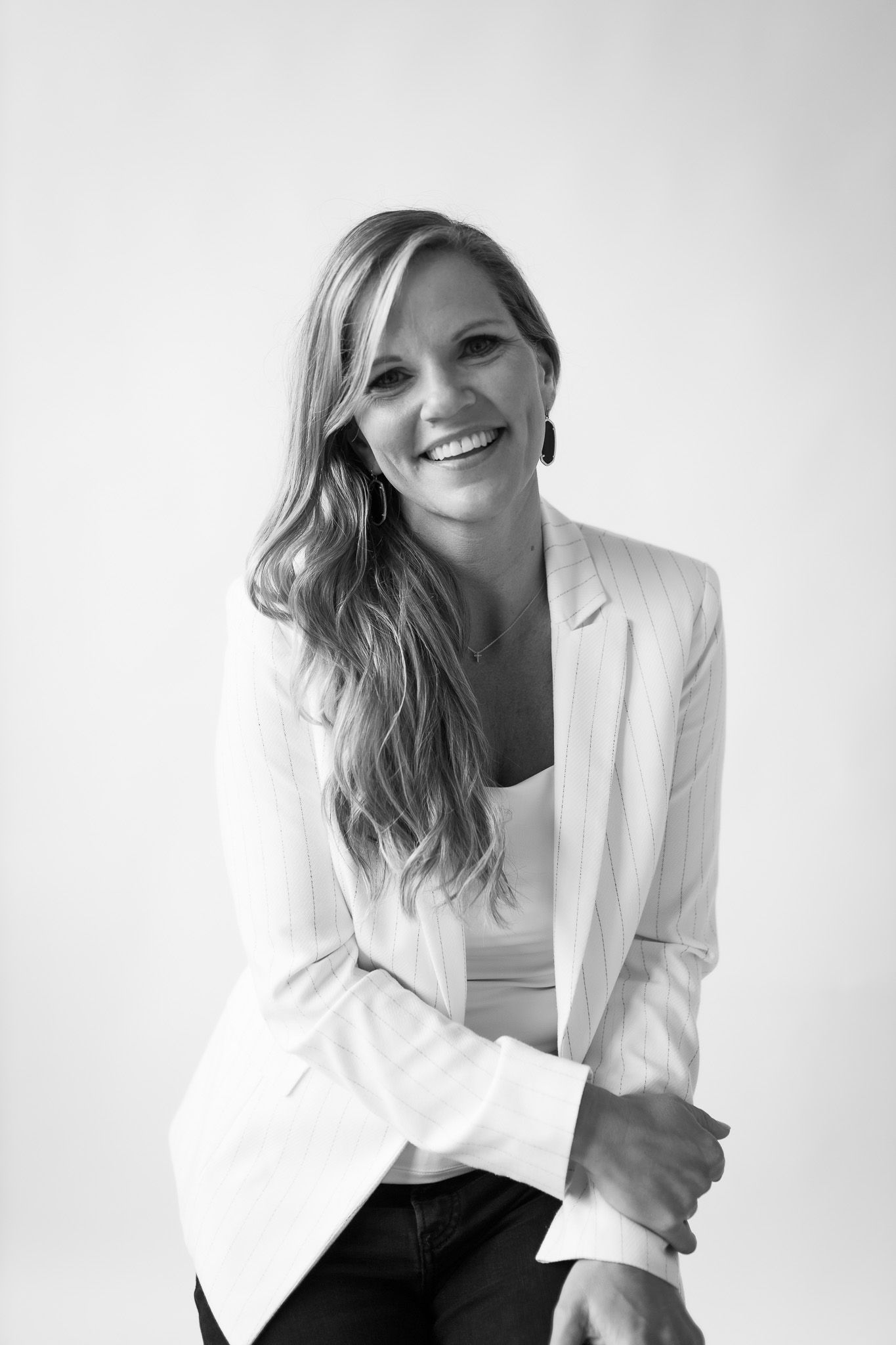 Smiling blonde woman in white blazer poses confidently in black and white professional portrait photo.