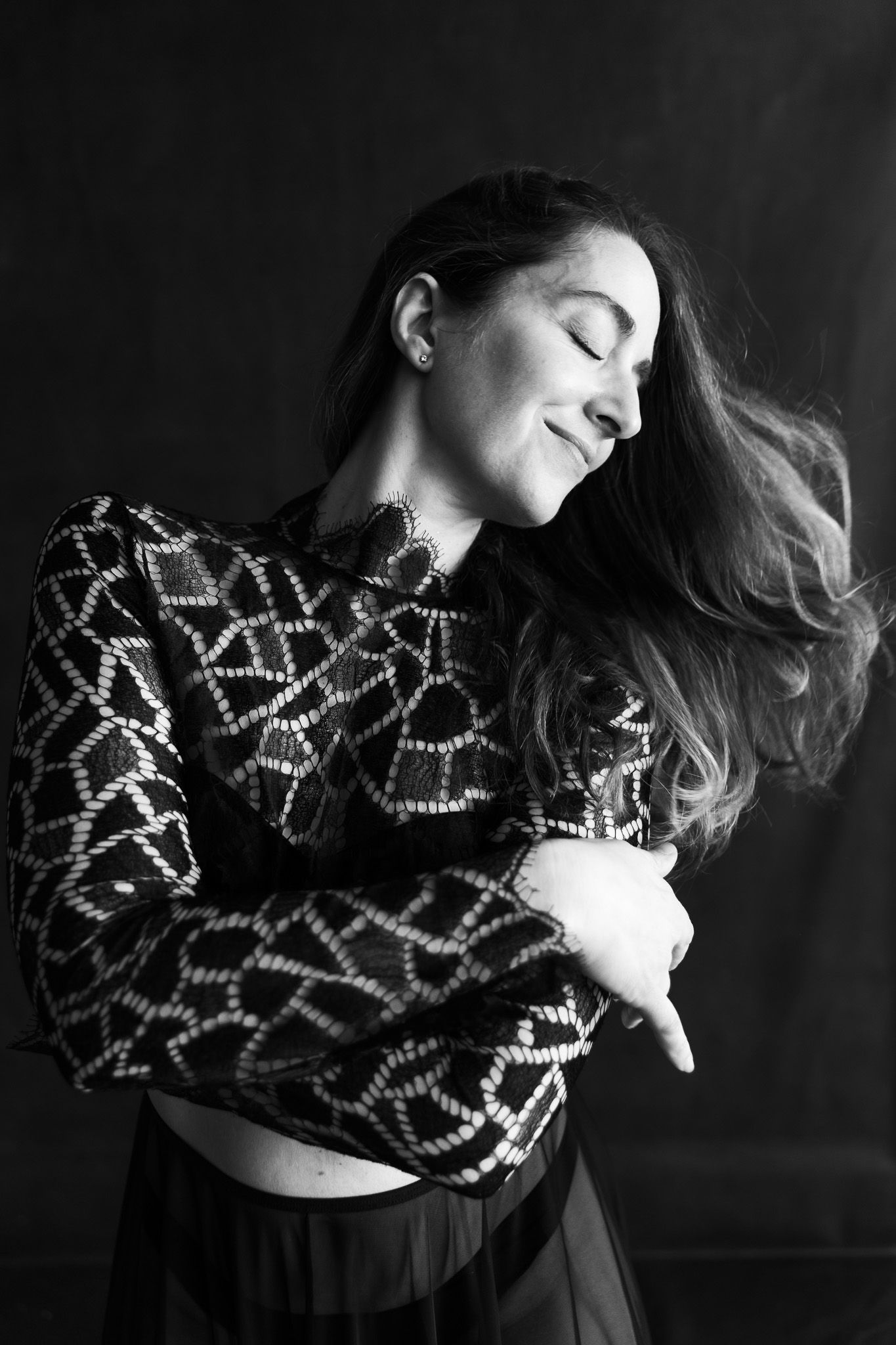 Woman in patterned black top with flowing hair, eyes closed, black and white studio photo.