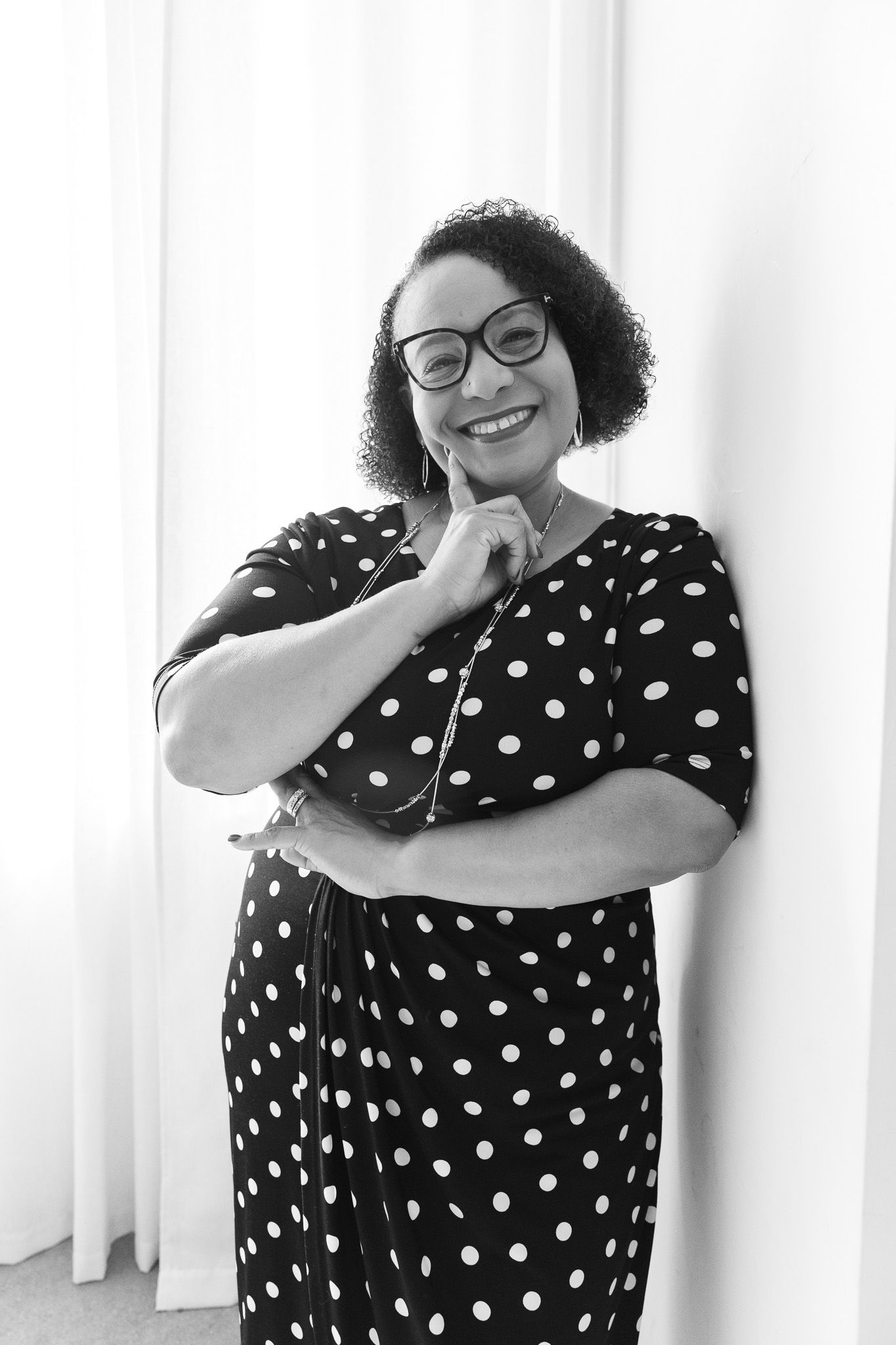 Smiling woman in polka dot dress and glasses posing confidently in a black and white portrait photo.