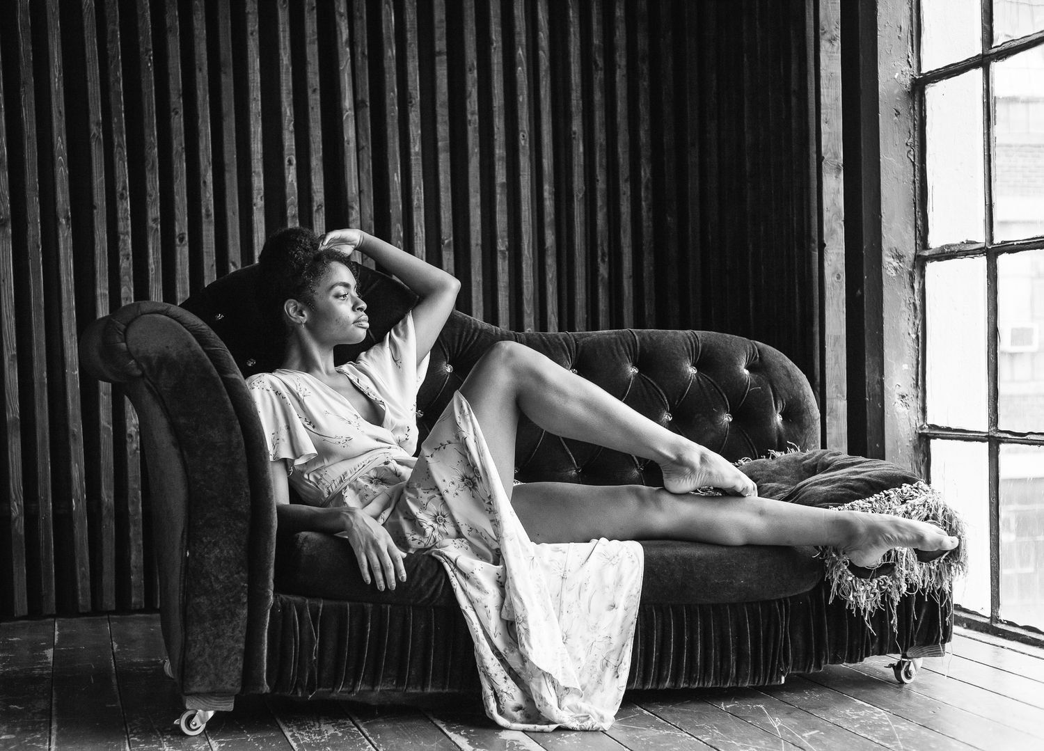Black and white portrait of woman in white dress reclining elegantly on vintage chaise lounge.