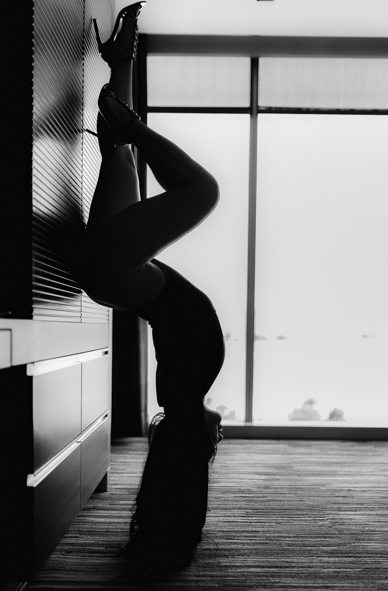 Silhouette of woman in heels poses against wall in dramatic black and white boudoir photography.