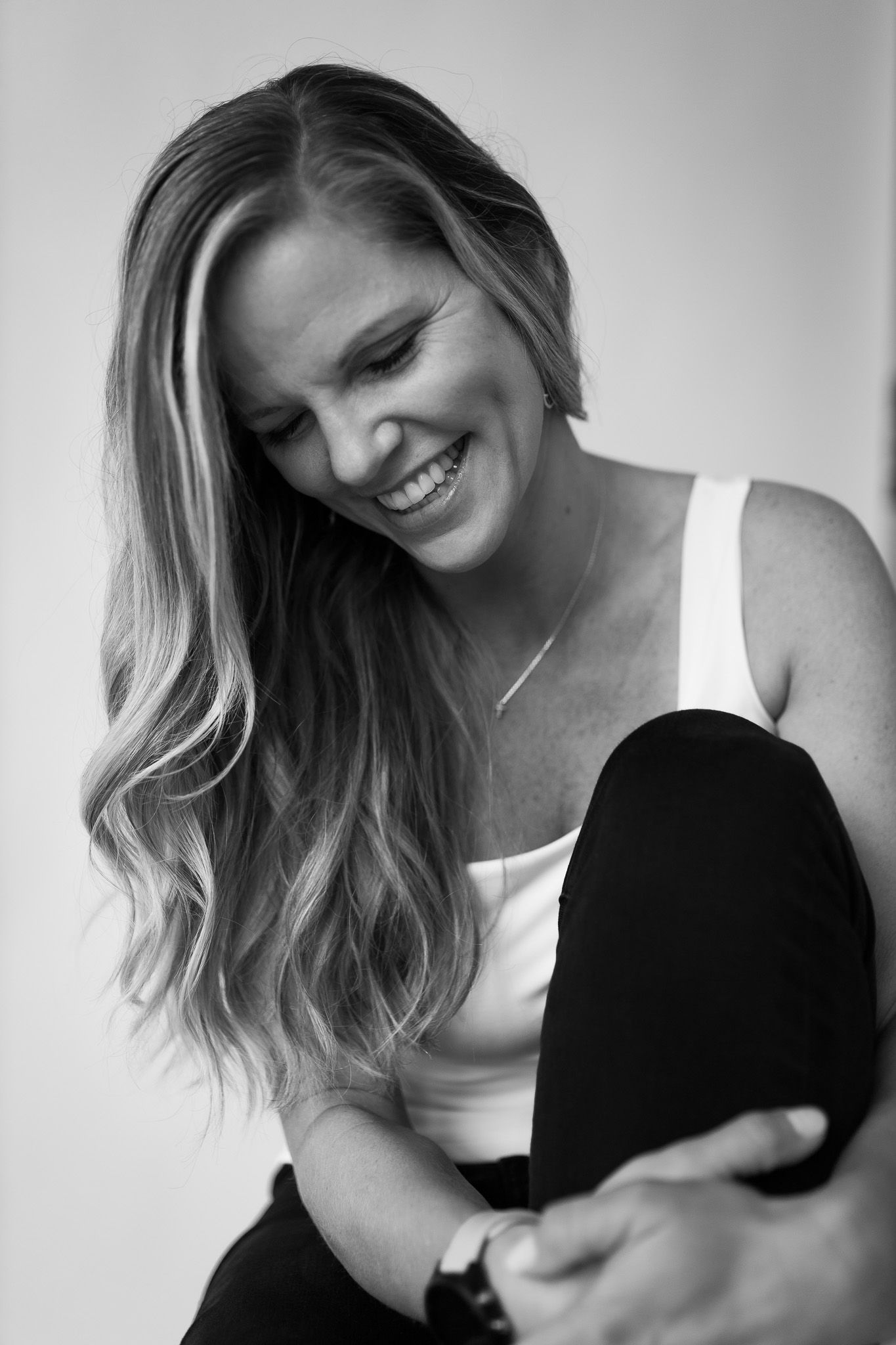 Smiling blonde woman with long wavy hair laughing joyfully in black and white portrait photo.