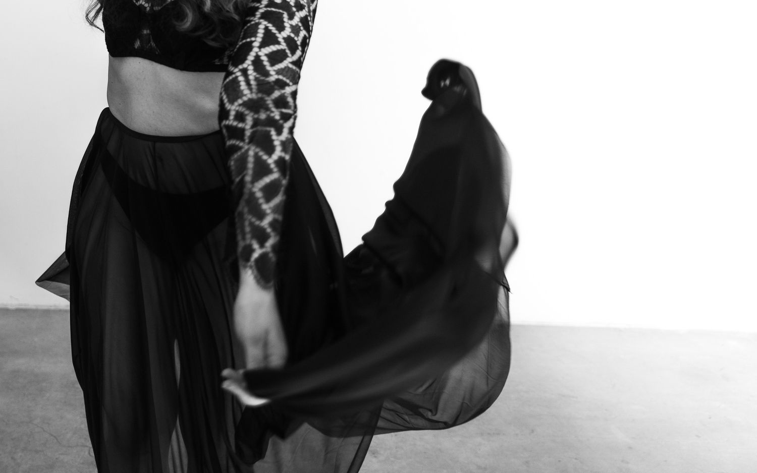Black and white photo of dancer in patterned top and flowing sheer black skirt in motion.