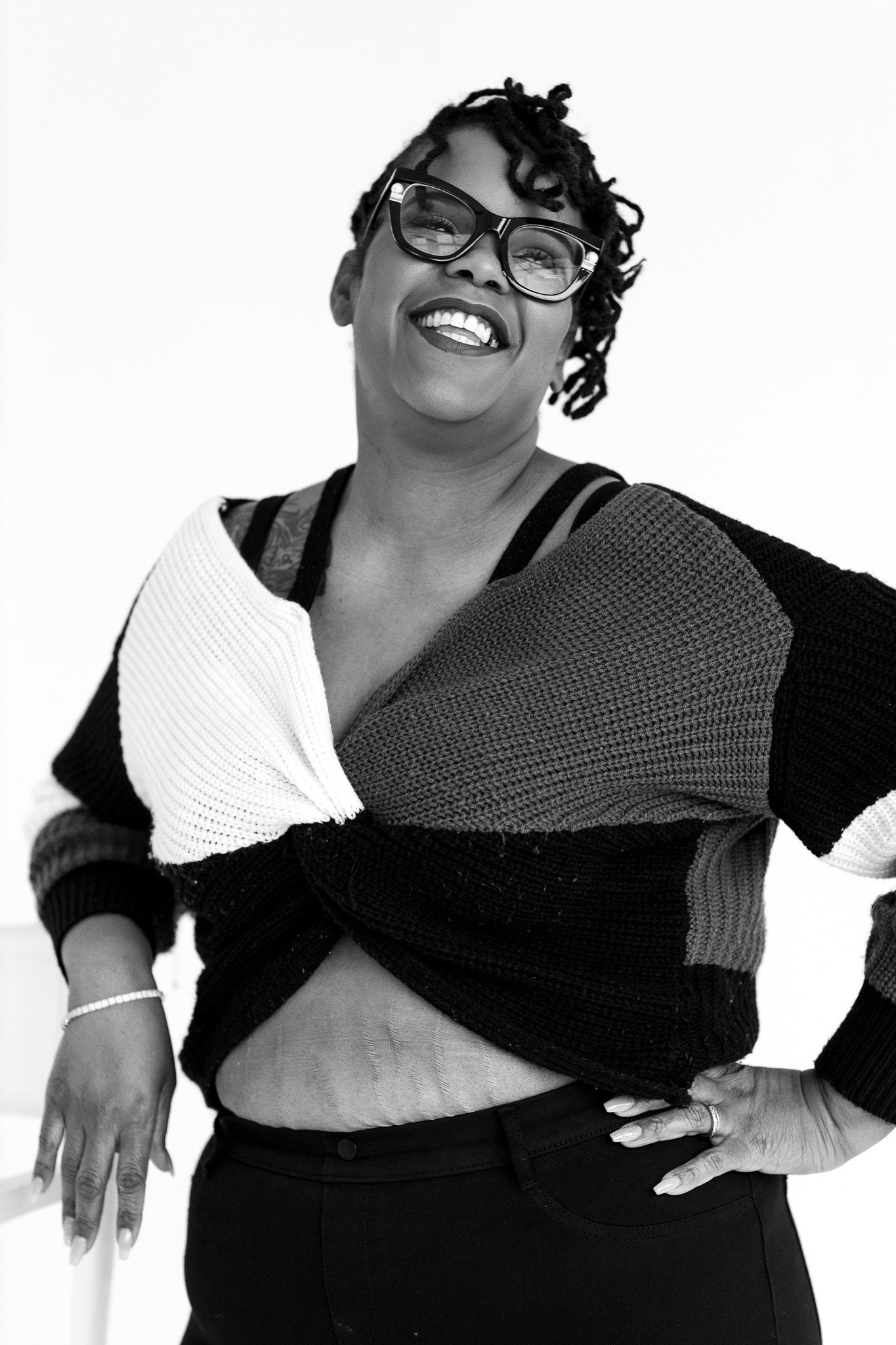 Black and white portrait of a smiling woman in glasses wearing a stylish wrap sweater, posing confidently.