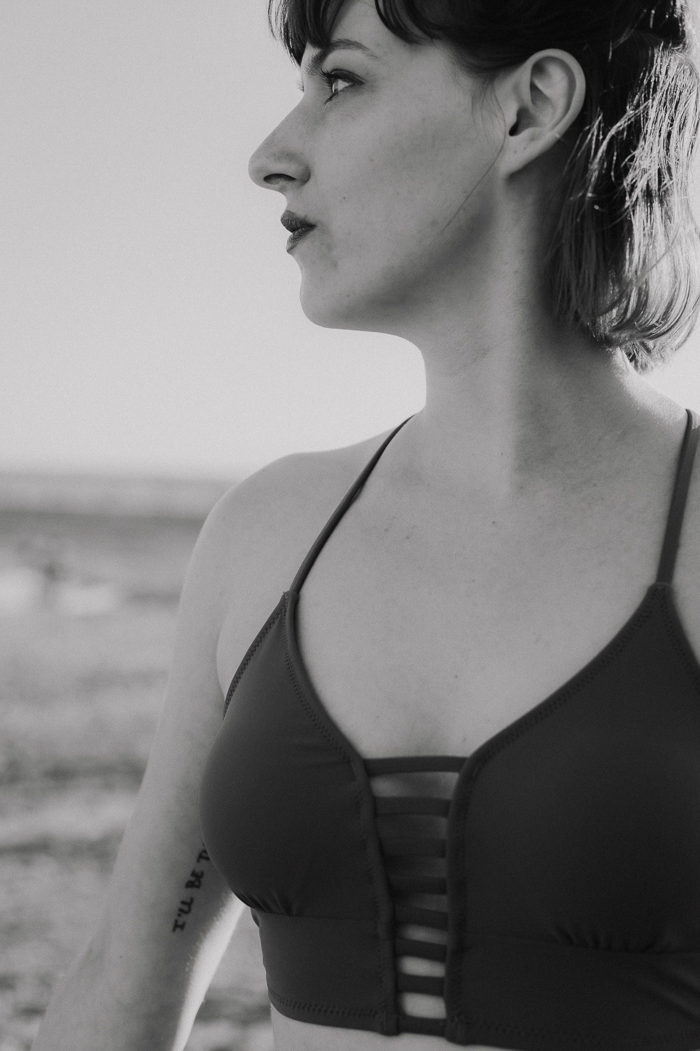 Black and white side profile portrait of a woman in a strappy sports bra at the beach.