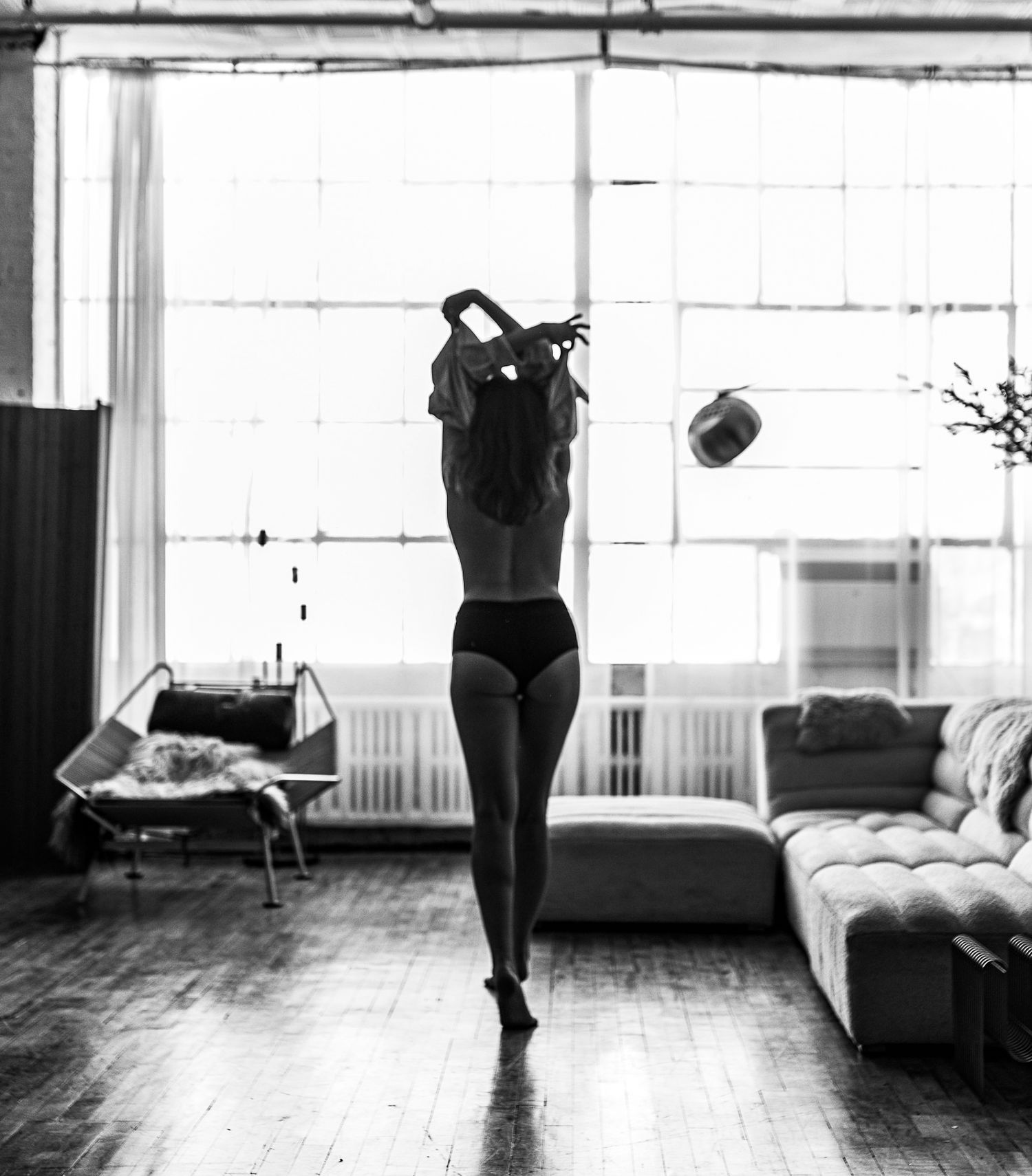 Monochrome shot of a woman removing her top in a spacious loft interior.