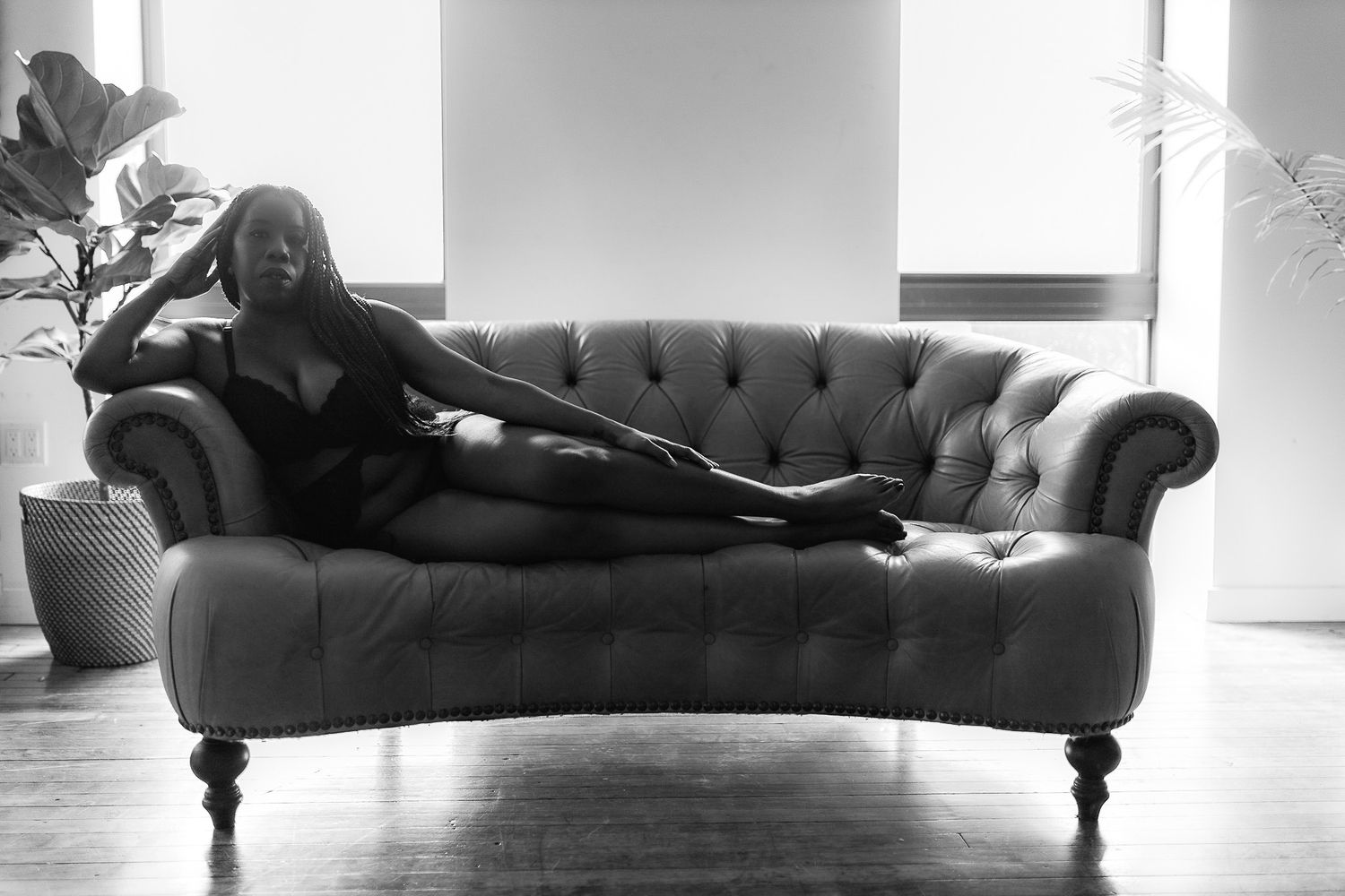 Black and white photo of a woman in lingerie reclining on a tufted sofa.