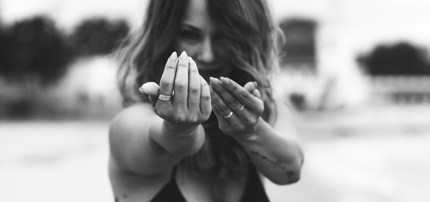 Black and white image of woman with rings extending both hands forward toward camera outdoors.