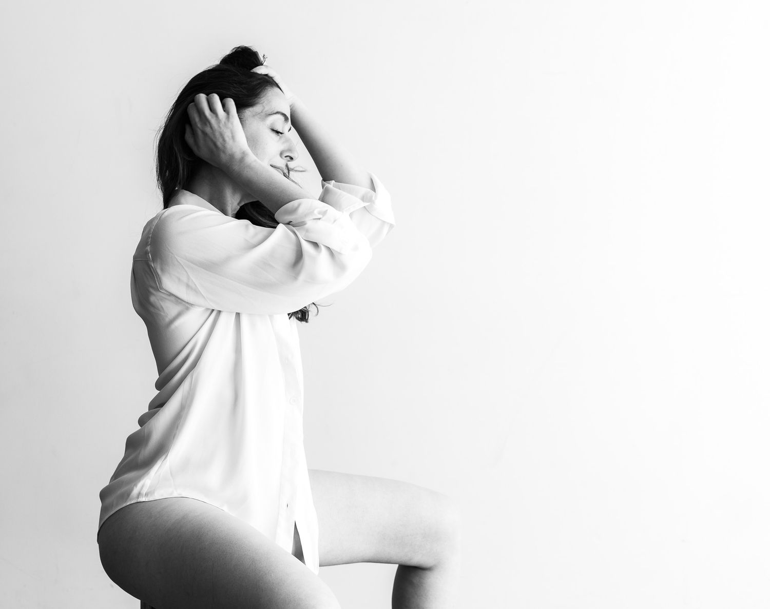 Black and white artistic photo of woman in white shirt with hands framing her face.