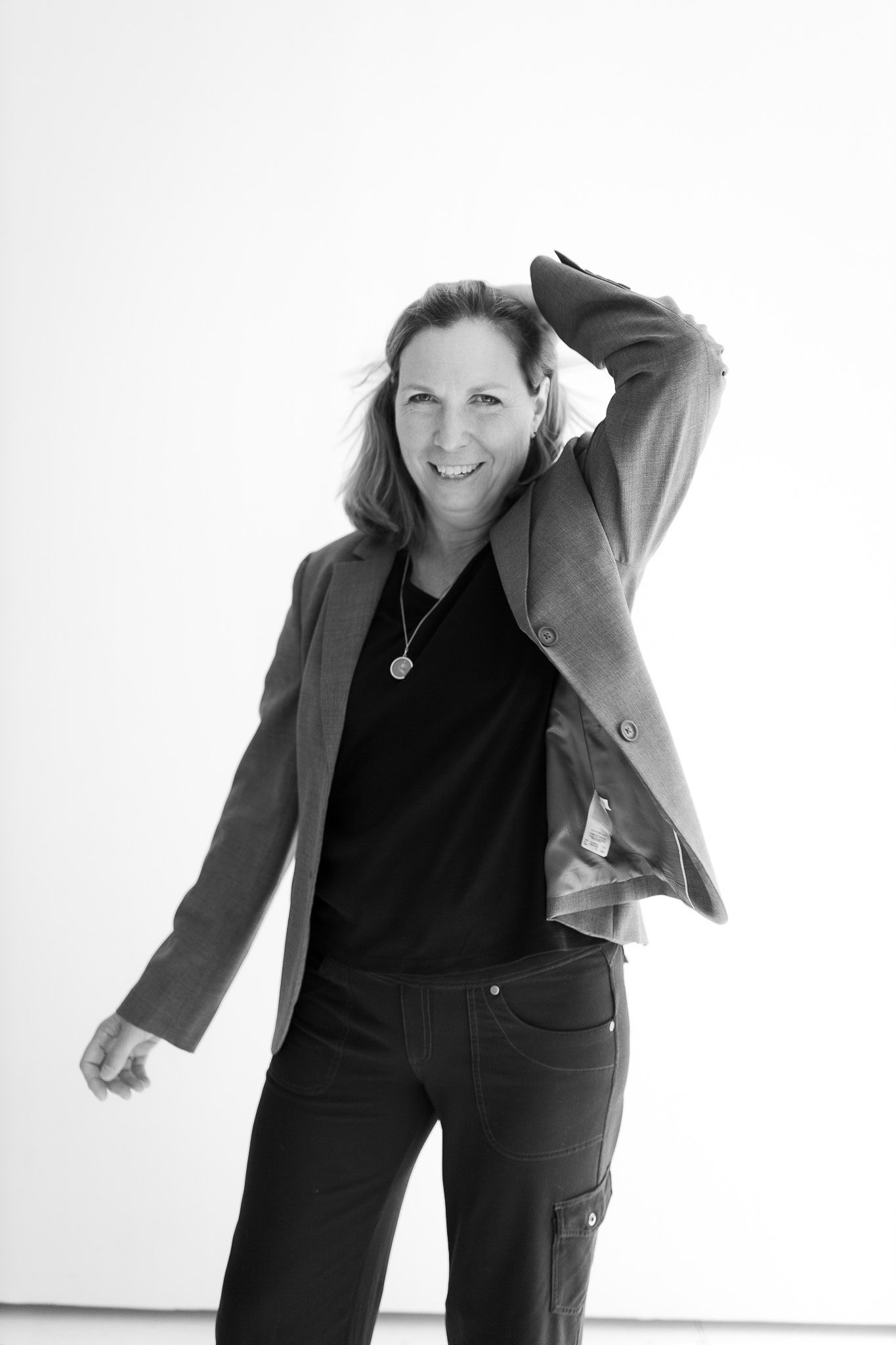 Woman in blazer and black top smiling and posing dynamically against white background.
