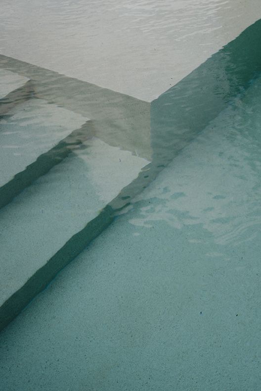 Abstract close-up of turquoise swimming pool steps with clear water reflections and geometric concrete edges.