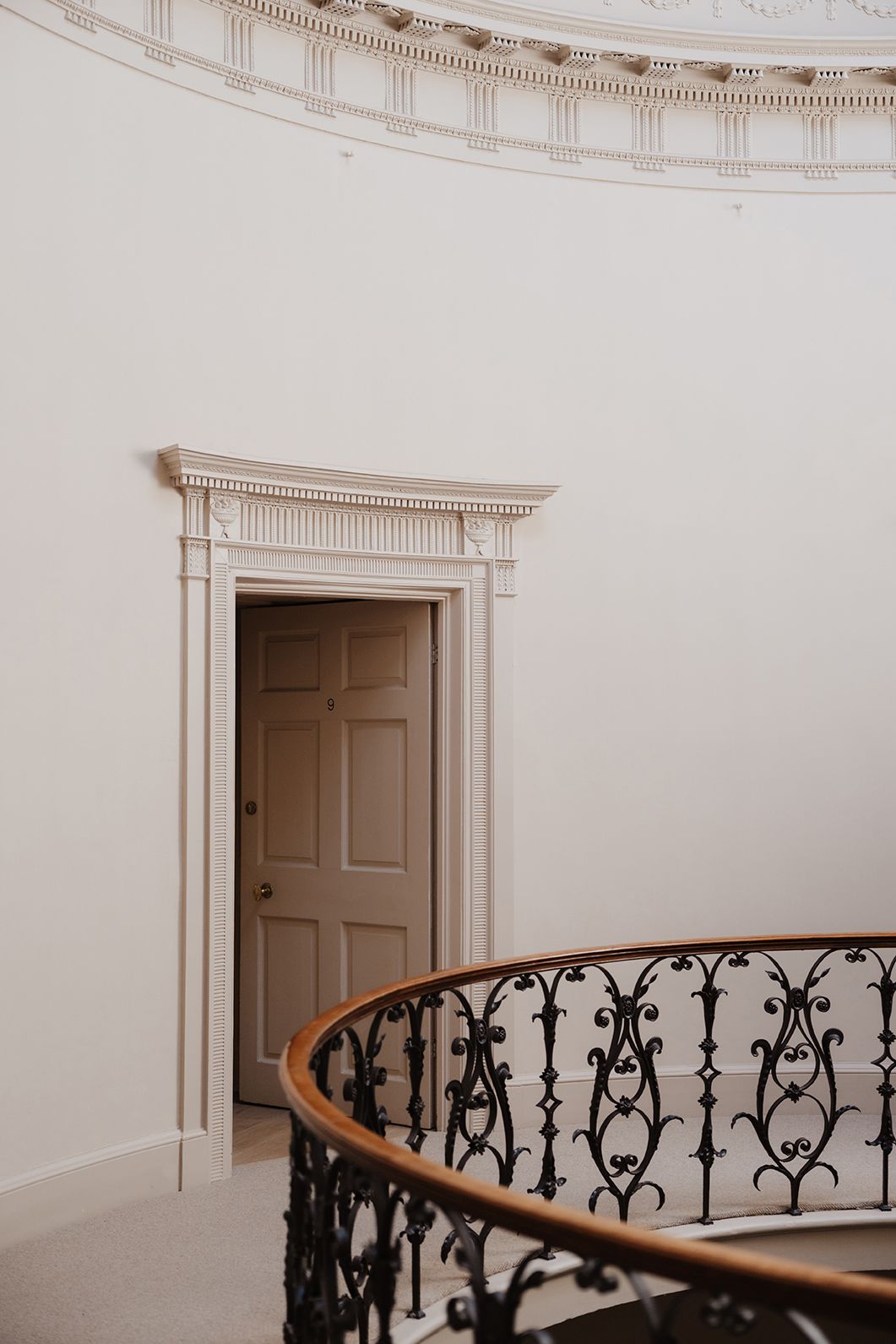 Grand curved staircase with ornate black iron balustrade and wooden handrail beneath decorative plaster ceiling medallion.