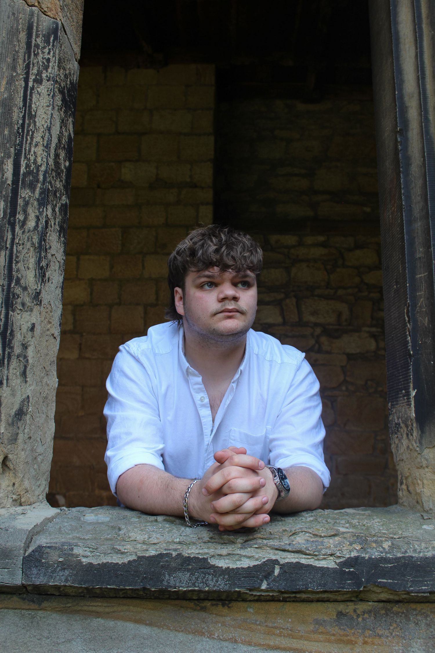 Editorial fashion portrait of a man leaning out of a window in Durham Cathedral. Wearing a white shirt.