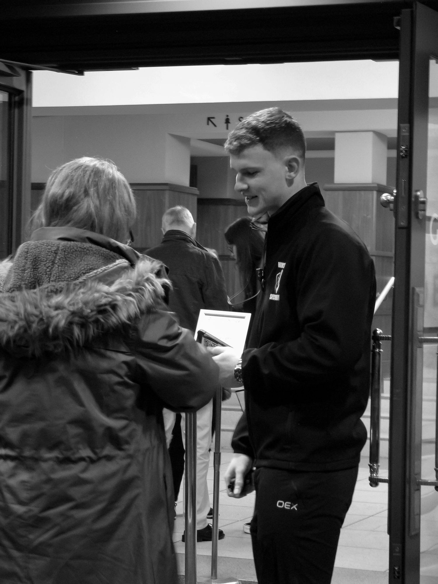 Action photo of a male security guard for Hinson Security Services scanning customer’s tickets at a theatre. Black and white.