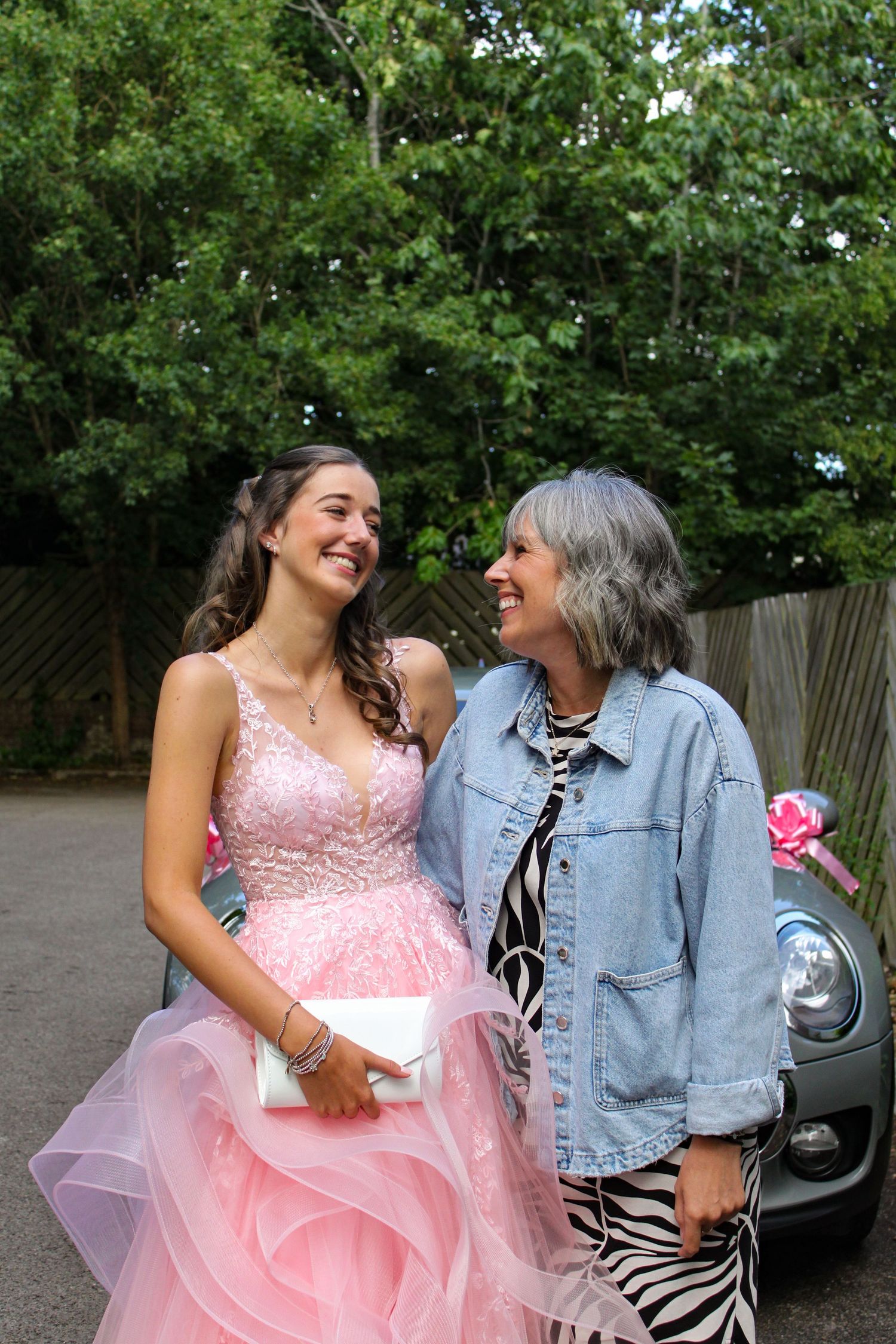 A mother and daughter laughing on the daughter’s prom day. Her prom dress is pink.